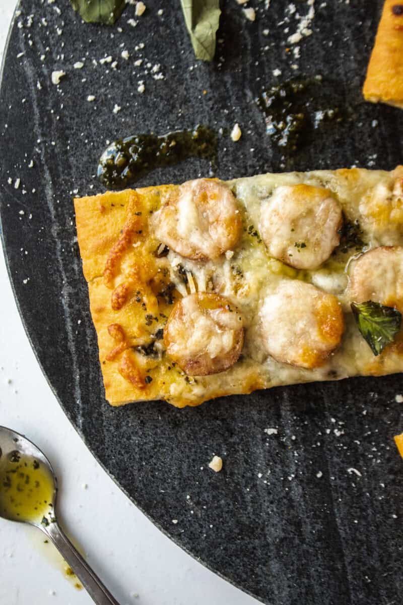 Close up of a chicken sausage and pesto flatbread on a platter.