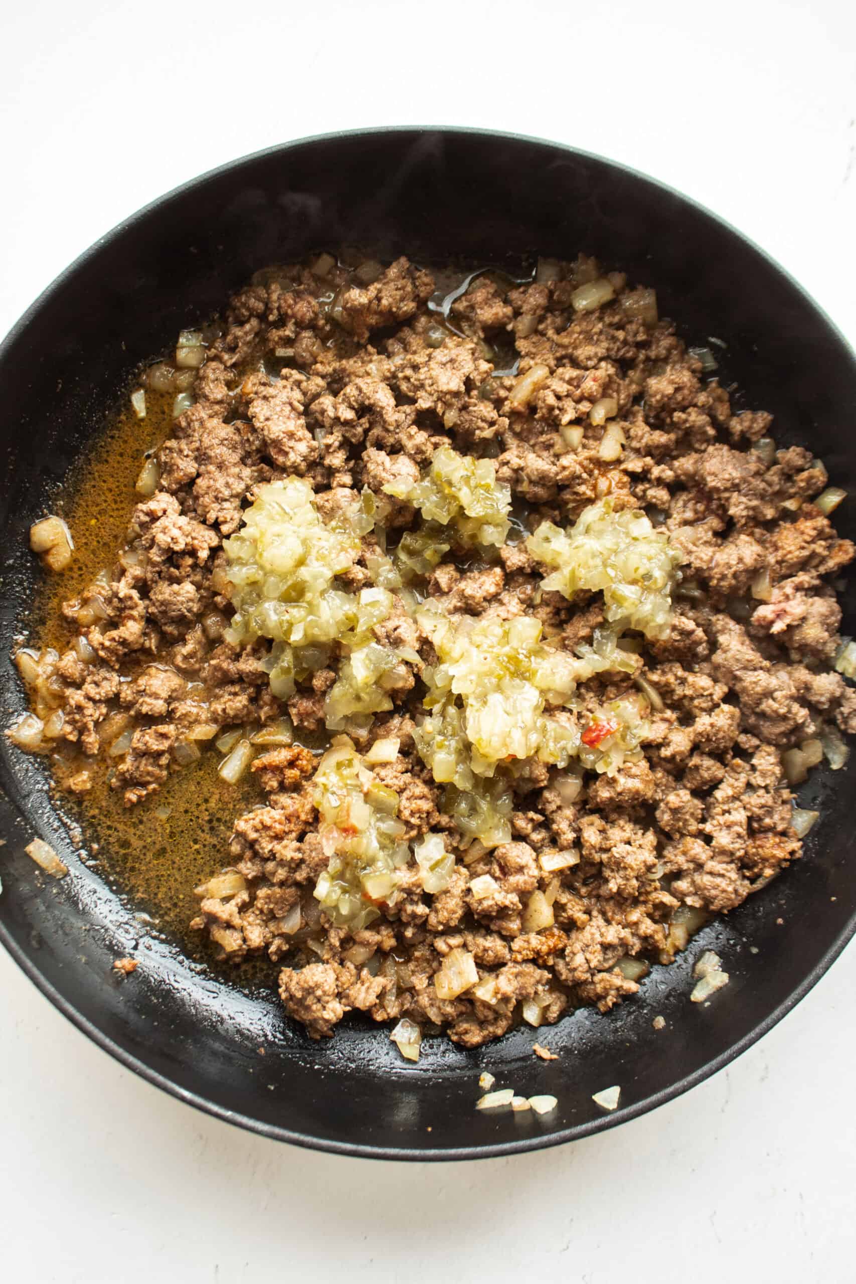 Dill relish added to a cast iron skillet of sauteed onions and ground beef.