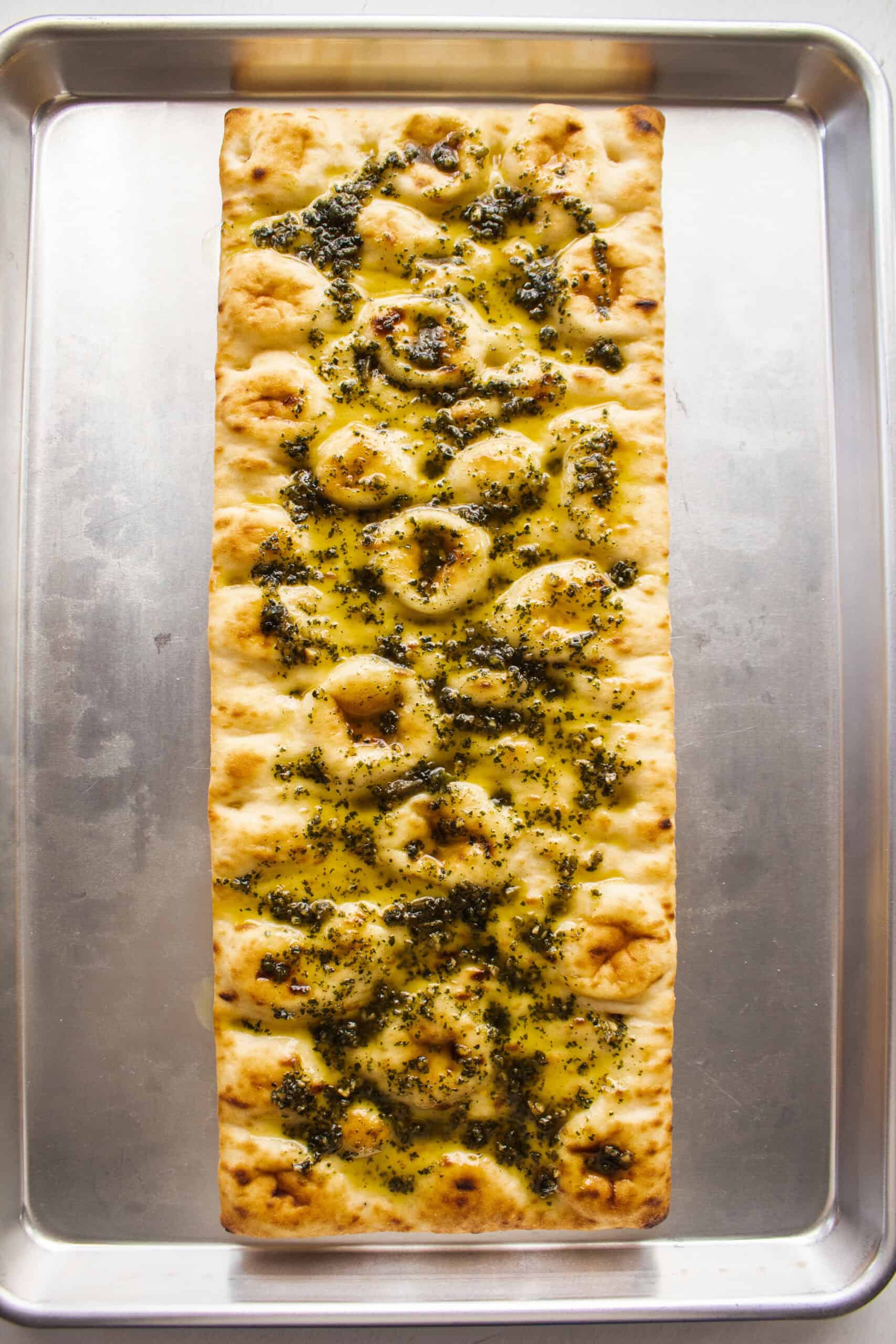 Pesto spread on a flatbread on a sheet pan.