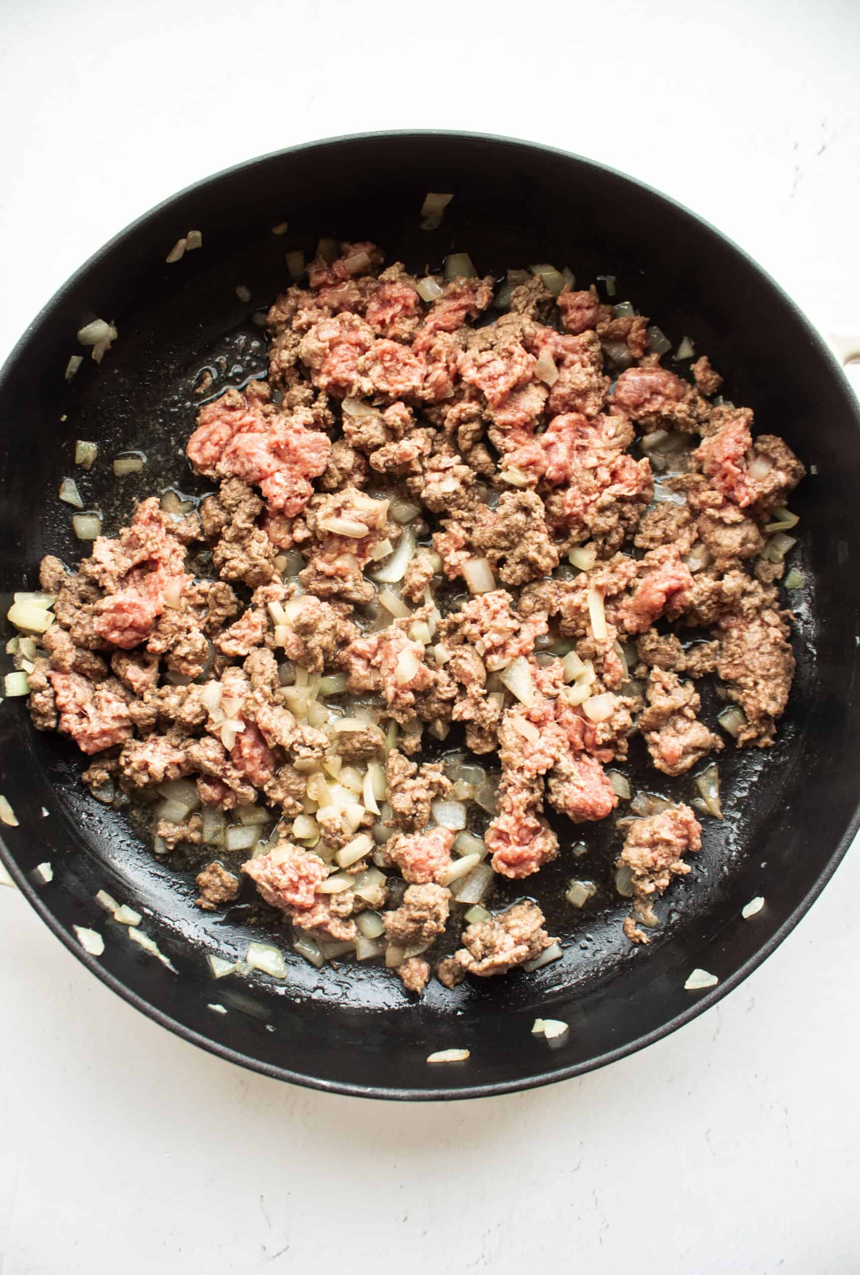 Sauteed onions and ground beef in a large cast iron skillet.