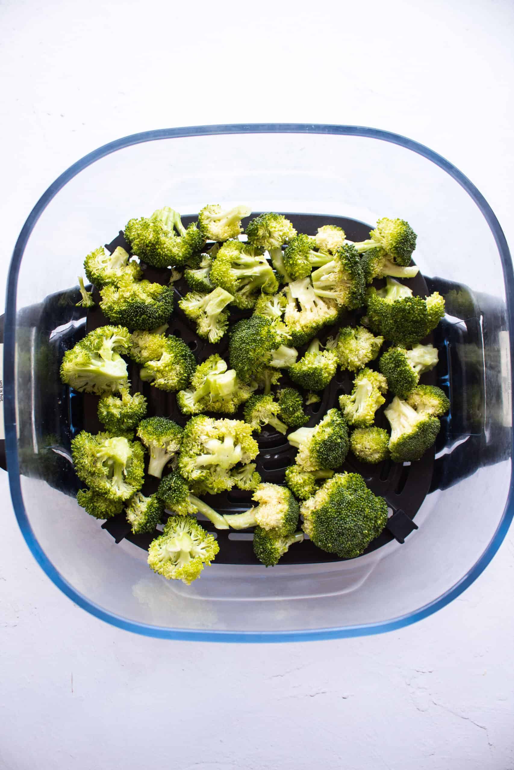 Seasoned broccoli in the base of an air fryer.