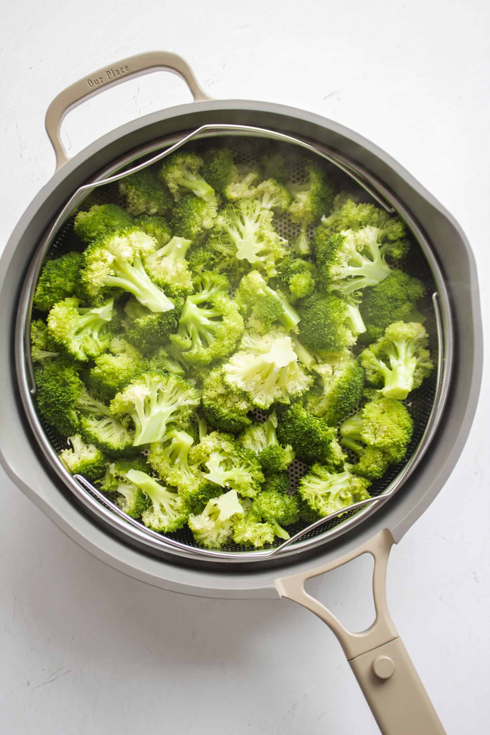 Blanched broccoli in a large frying pan with a colander.