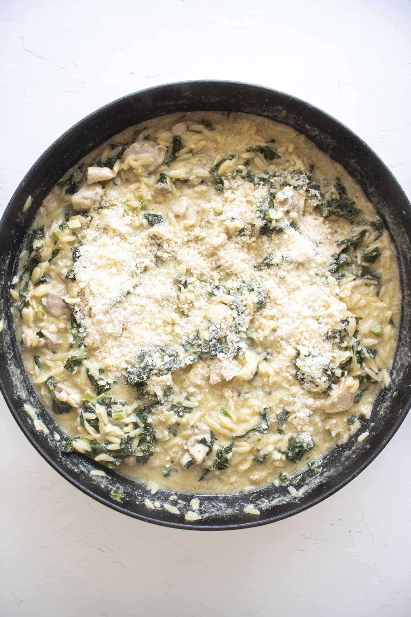 Cooked orzo with chicken and kale in a cast iron skillet with added grated parmesan cheese.