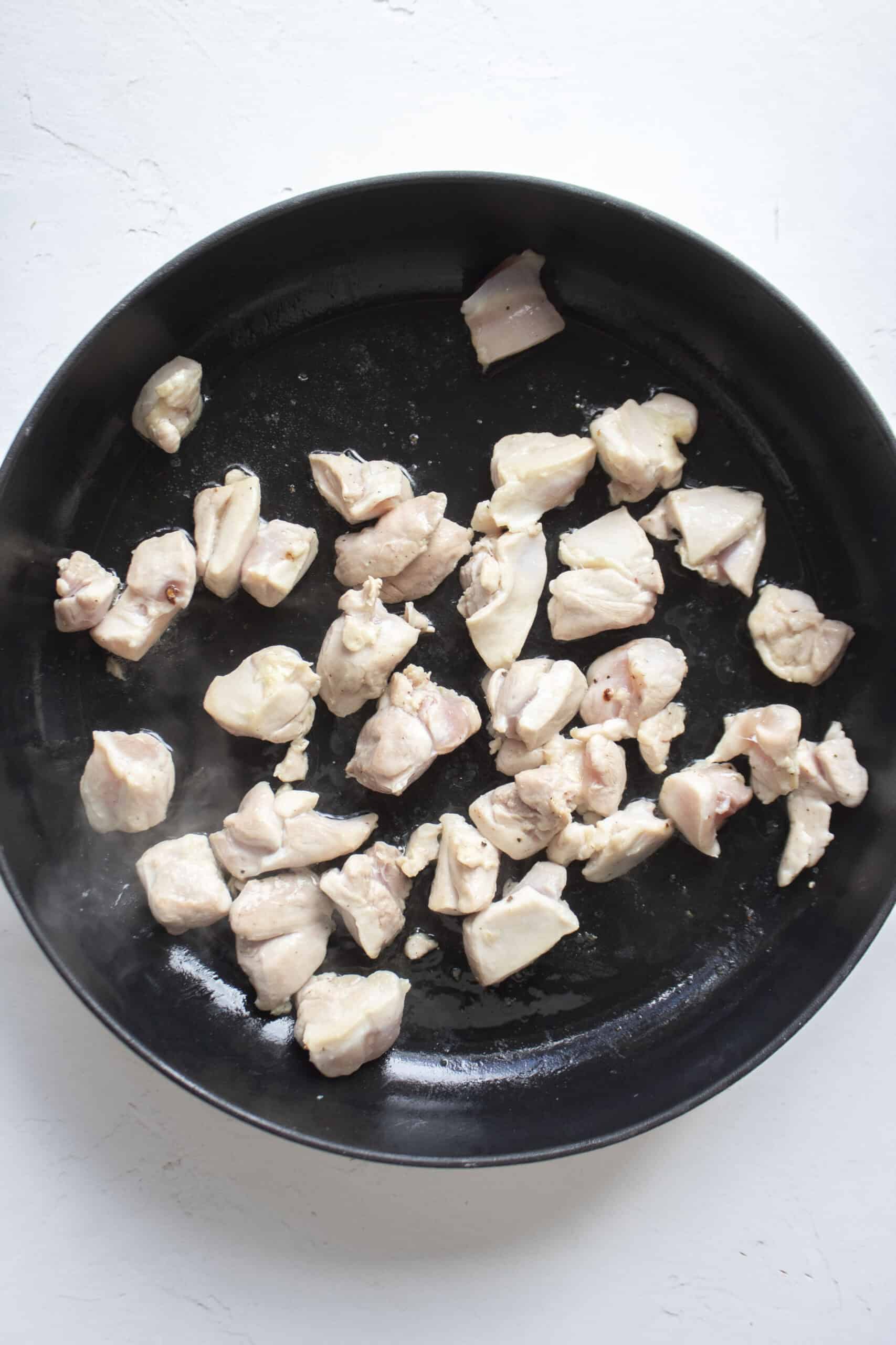 Diced chicken thighs in a large cast iron skillet with olive oil, salt, and pepper.