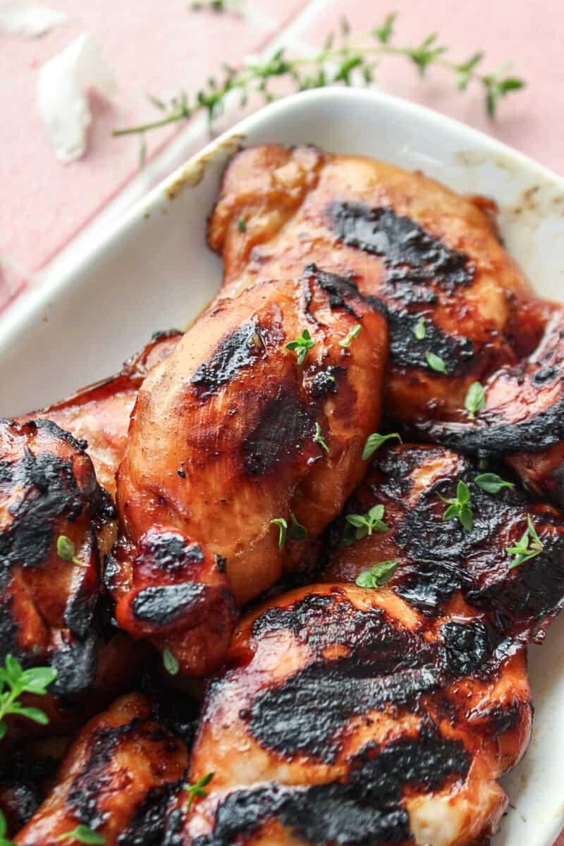 Close up of a grilled teriyaki chicken thigh on a plate topped with thyme.
