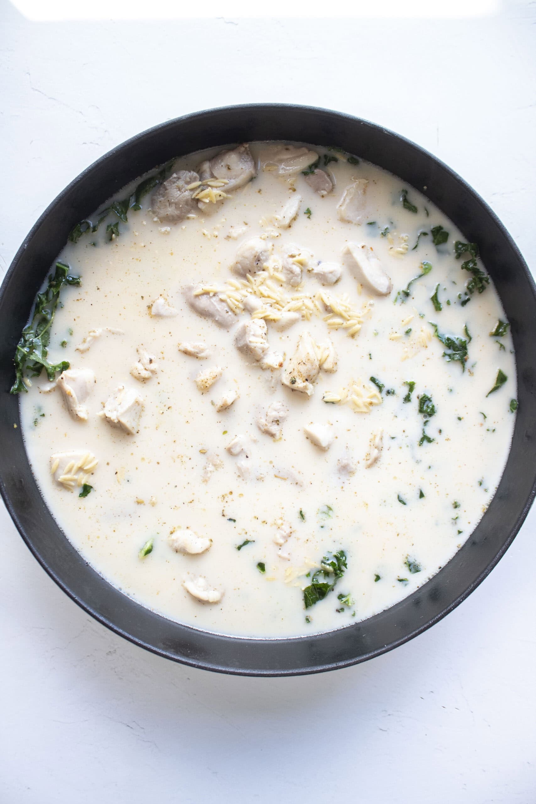 Milk, chicken broth, and dried orzo added to the cast iron skillet with kale and chicken.