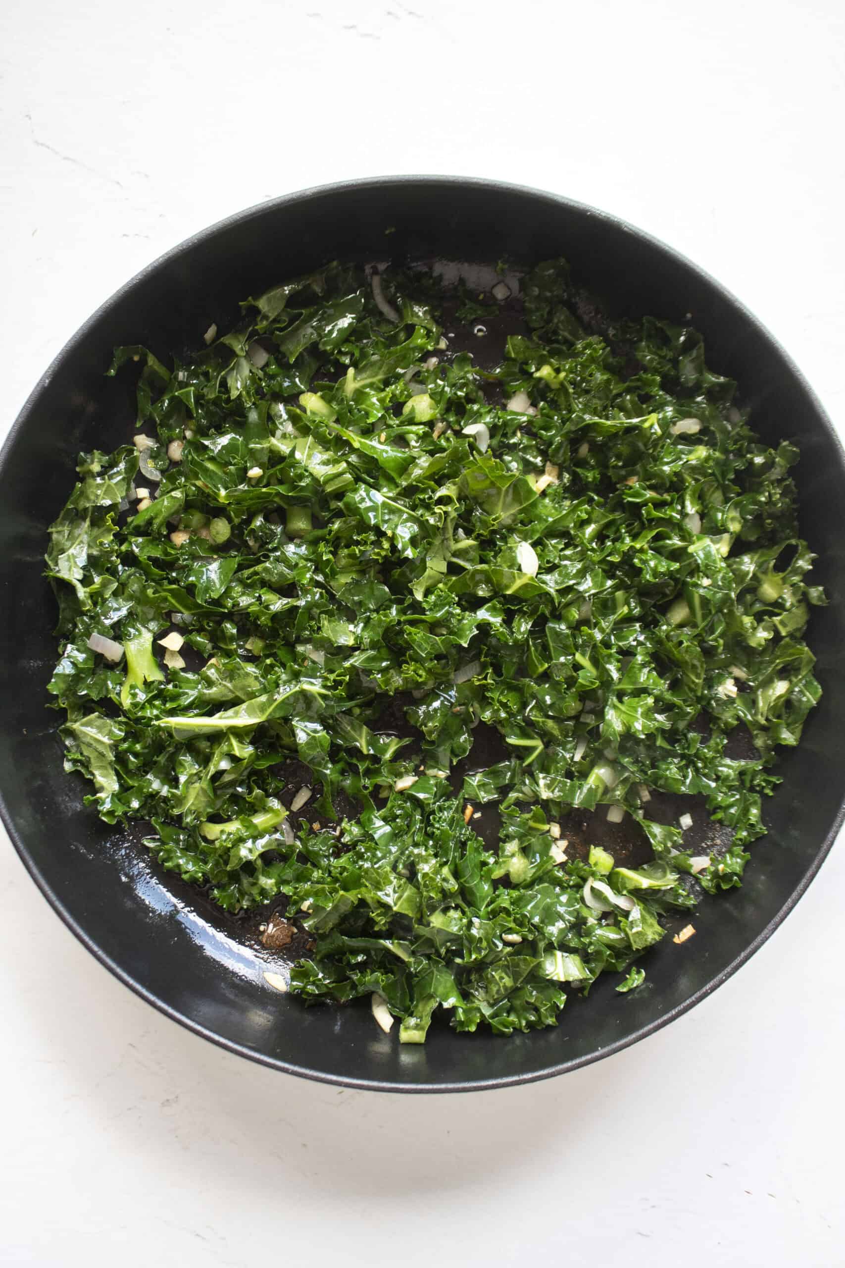 Shredded kale in a cast iron skillet with shallots and minced garlic.