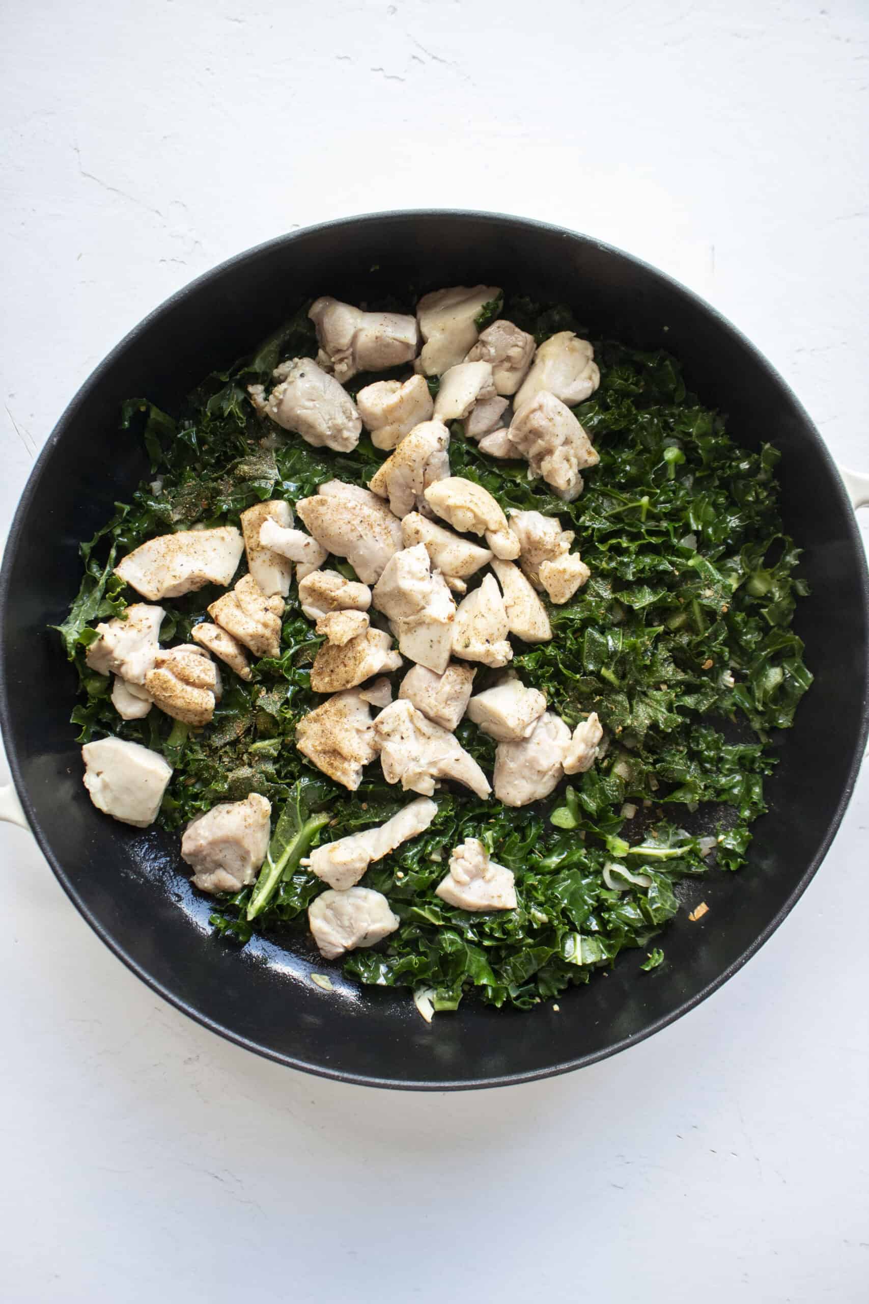 Shredded kale in a cast iron skillet with shallots and minced garlic with chicken added back in.