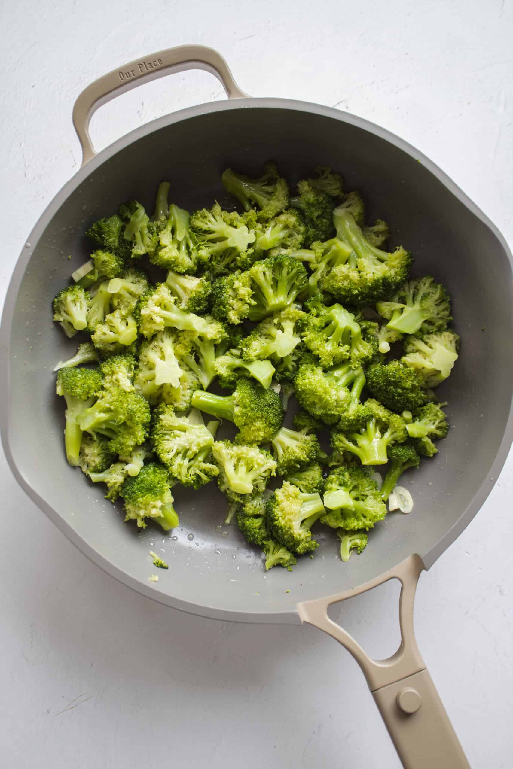 Steamed broccoli florets being sautéed in olive oil with sliced garlic.