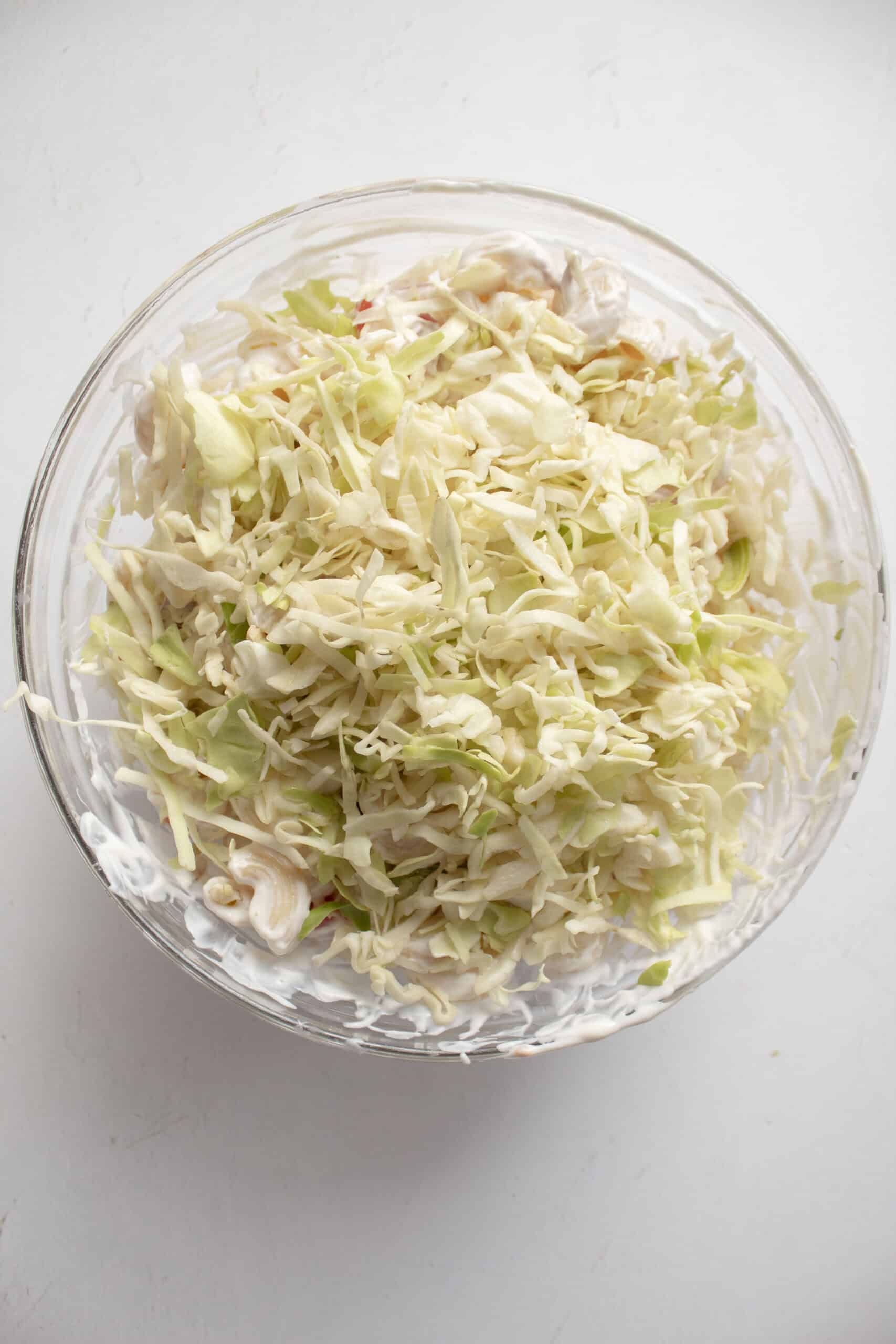 Shredded lettuce with and pepper on top of a bowl with macaroni, diced bacon, tomatoes, and a greek yogurt and mayo mixture.