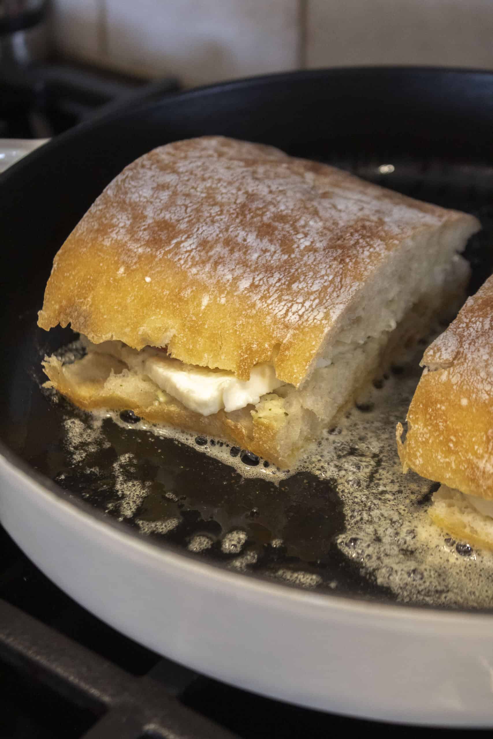 An heirloom tomato and mozzarella ciabatta getting toasted in butter in a cast iron pan.