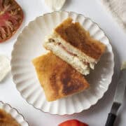 An heirloom tomato mozzarella ciabatta cut in half and stacked on each other on a scalloped plate.
