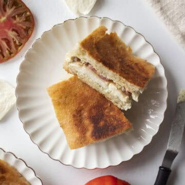 An heirloom tomato mozzarella ciabatta cut in half and stacked on each other on a scalloped plate.