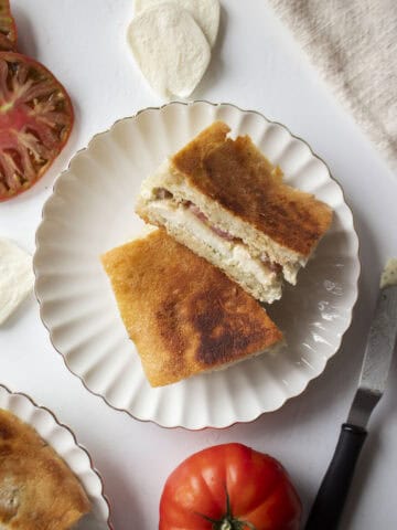 An heirloom tomato mozzarella ciabatta cut in half and stacked on each other on a scalloped plate.