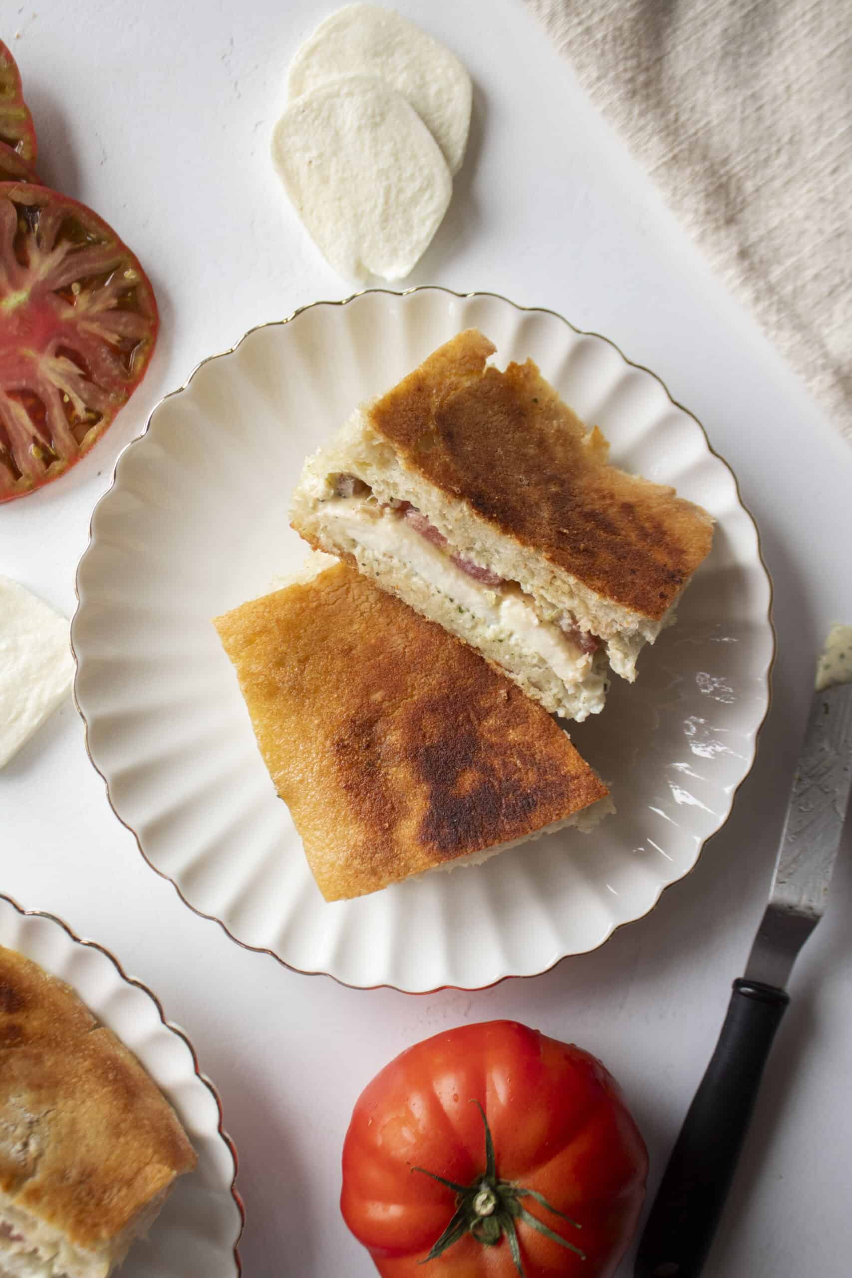 An heirloom tomato mozzarella ciabatta cut in half and stacked on each other on a scalloped plate.