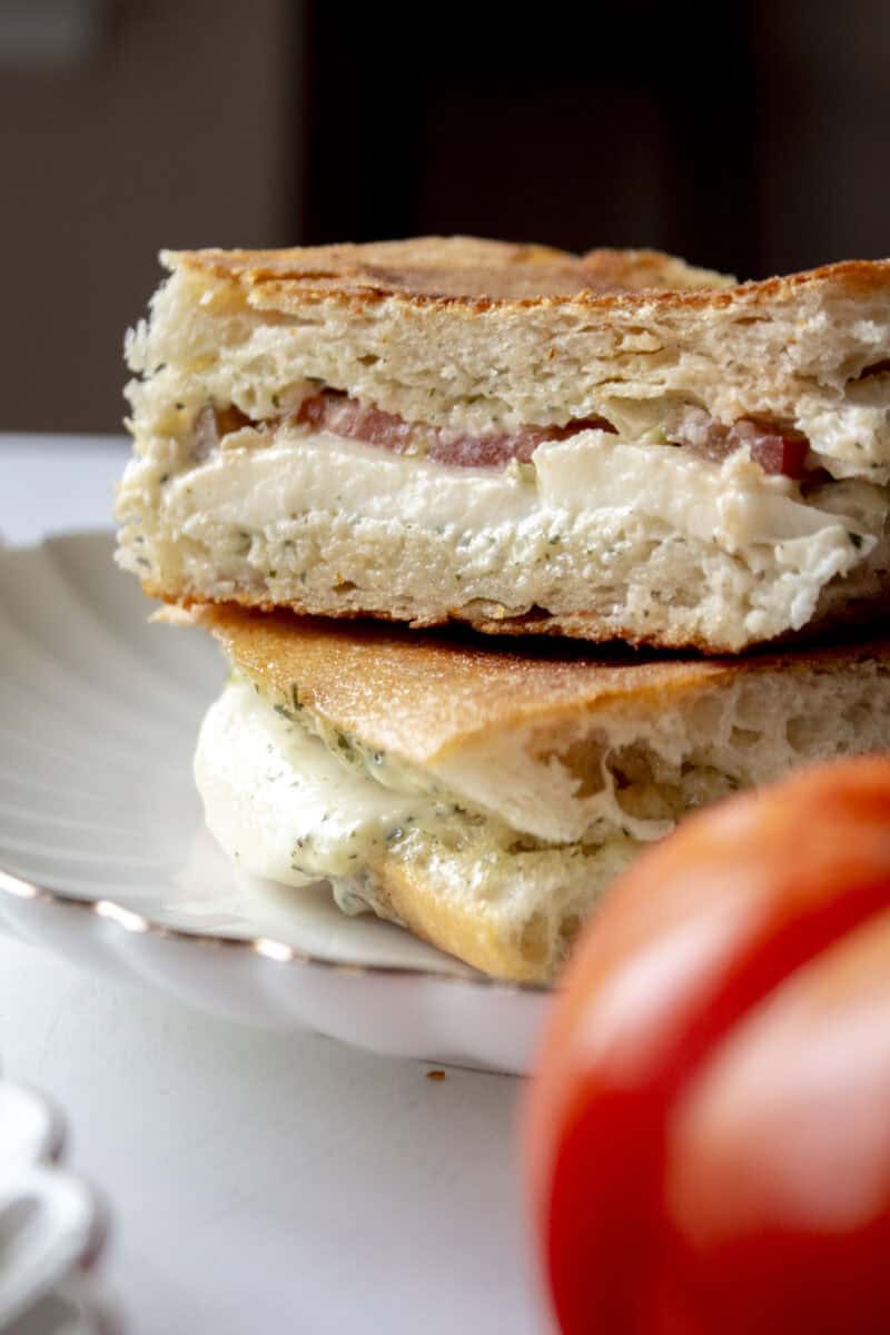 Close up of an heirloom tomato mozzarella ciabatta cut in half and stacked on each other on a scalloped plate.