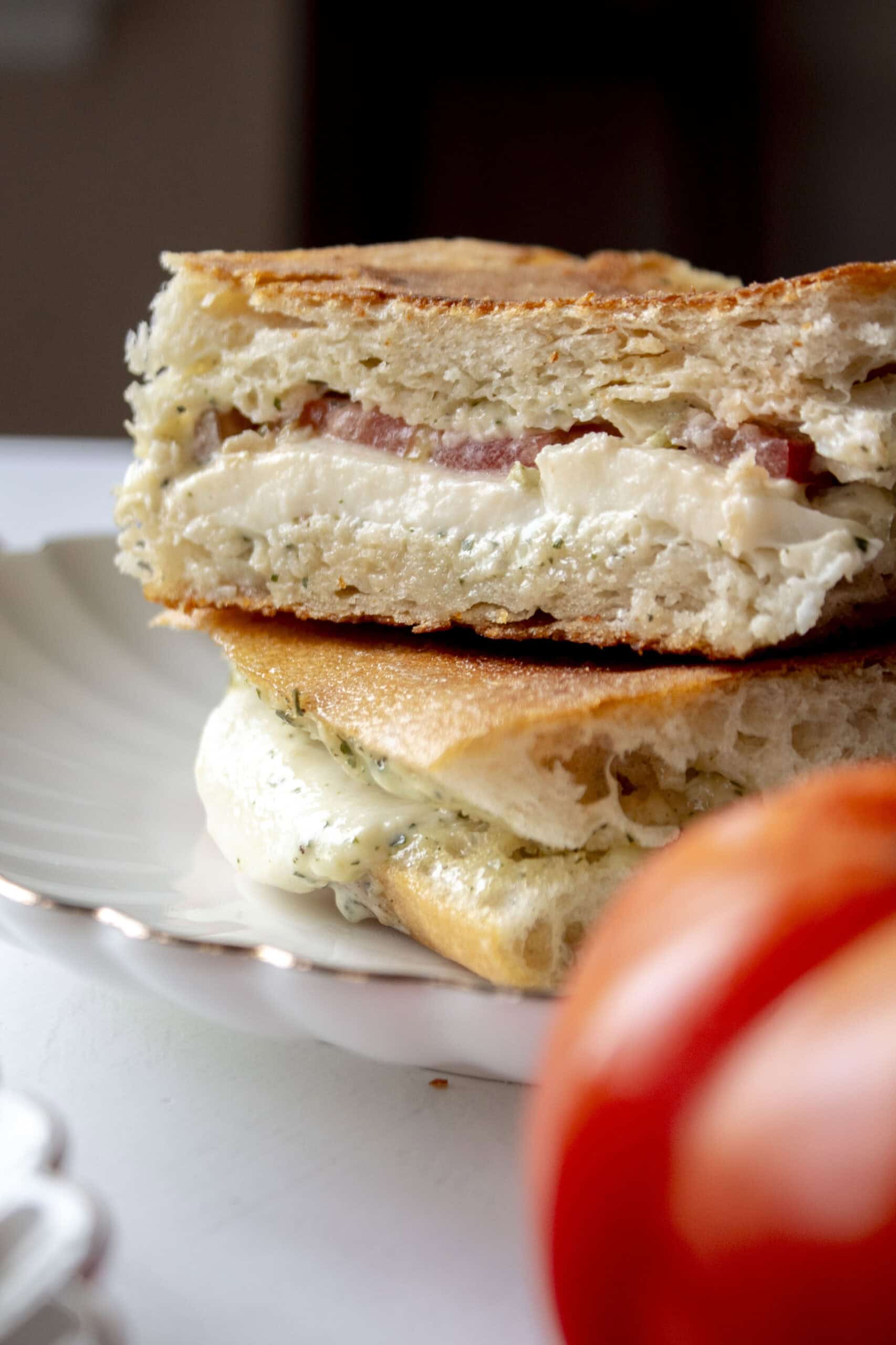 Close up of an heirloom tomato mozzarella ciabatta cut in half and stacked on each other on a scalloped plate.