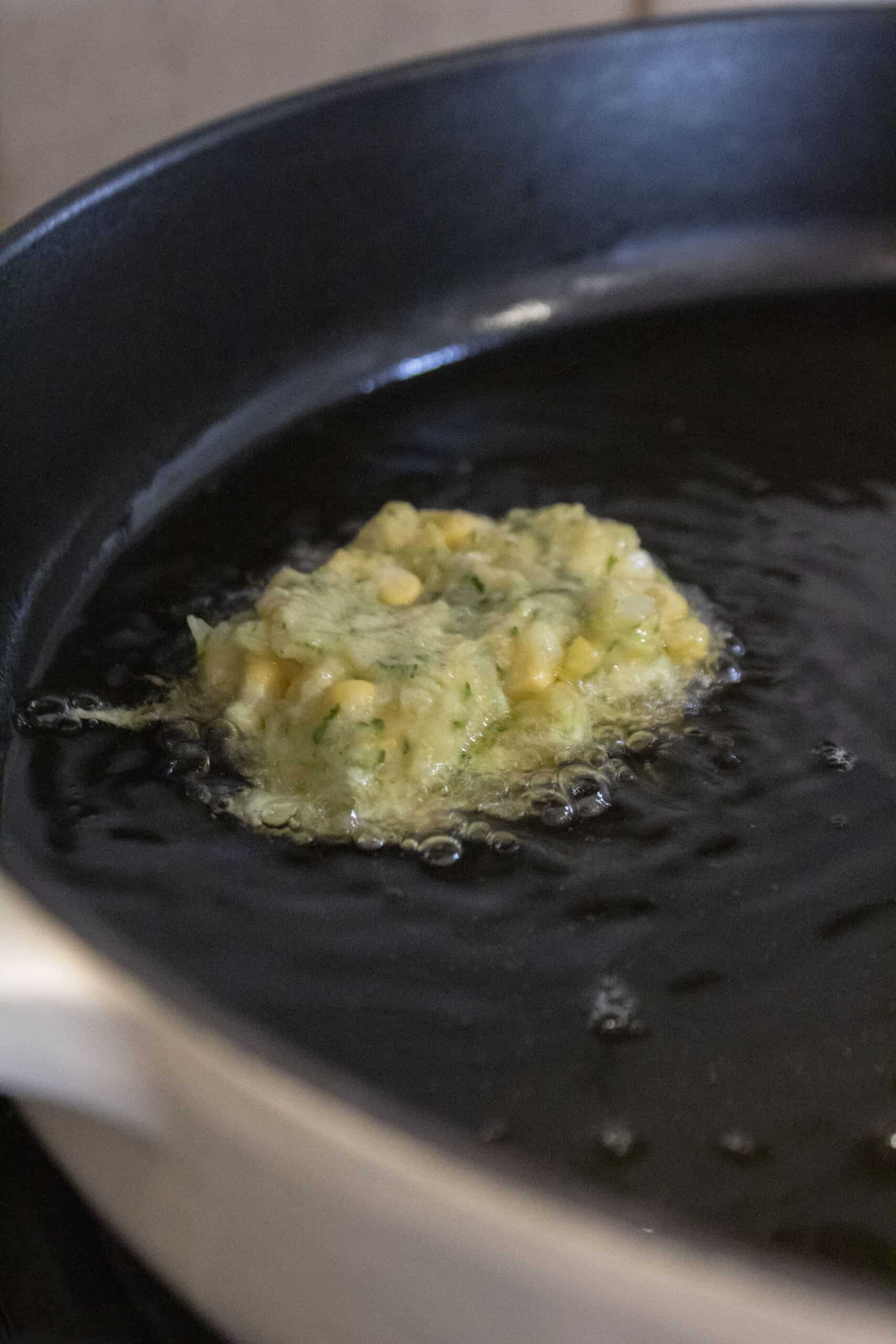 Corn and zucchini fritter batter frying in a cast iron skillet in olive oil.