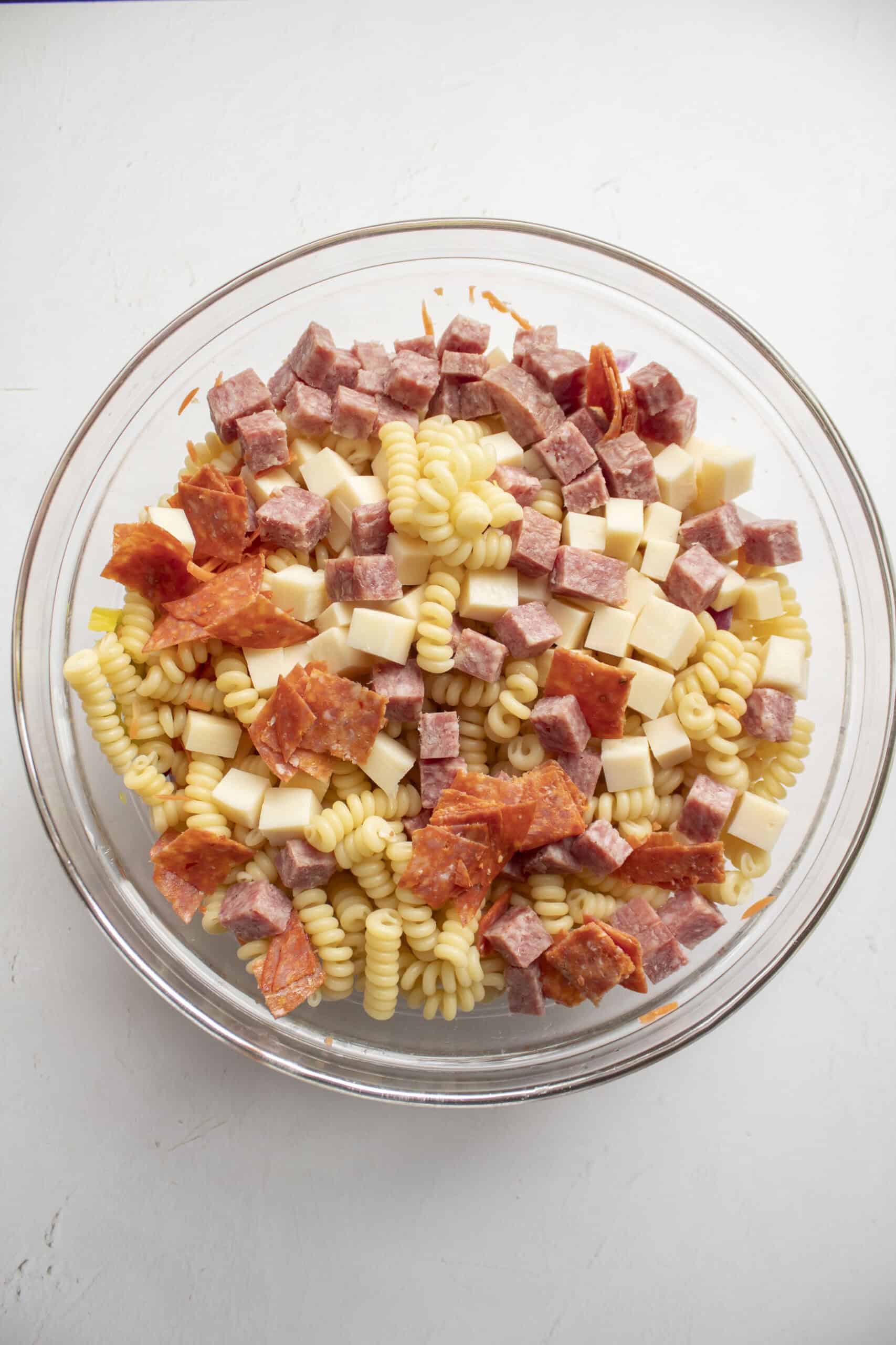 Pasta with shredded carrots, red onion, pepperoncini topped with cubed deli meats and cubed provolone cheese.