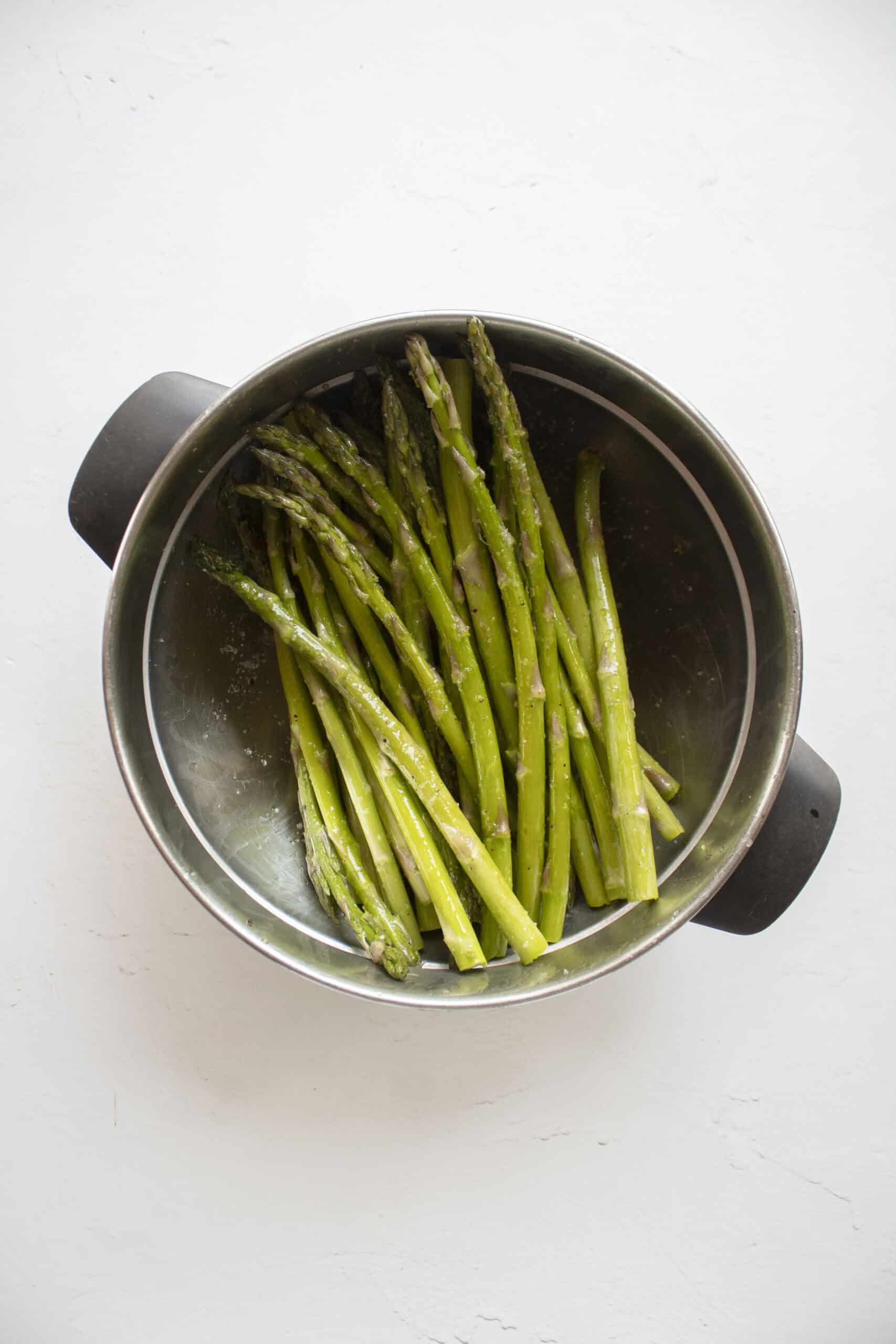 Trimmed asparagus in a mixing bowl with olive oil, salt, and pepper.
