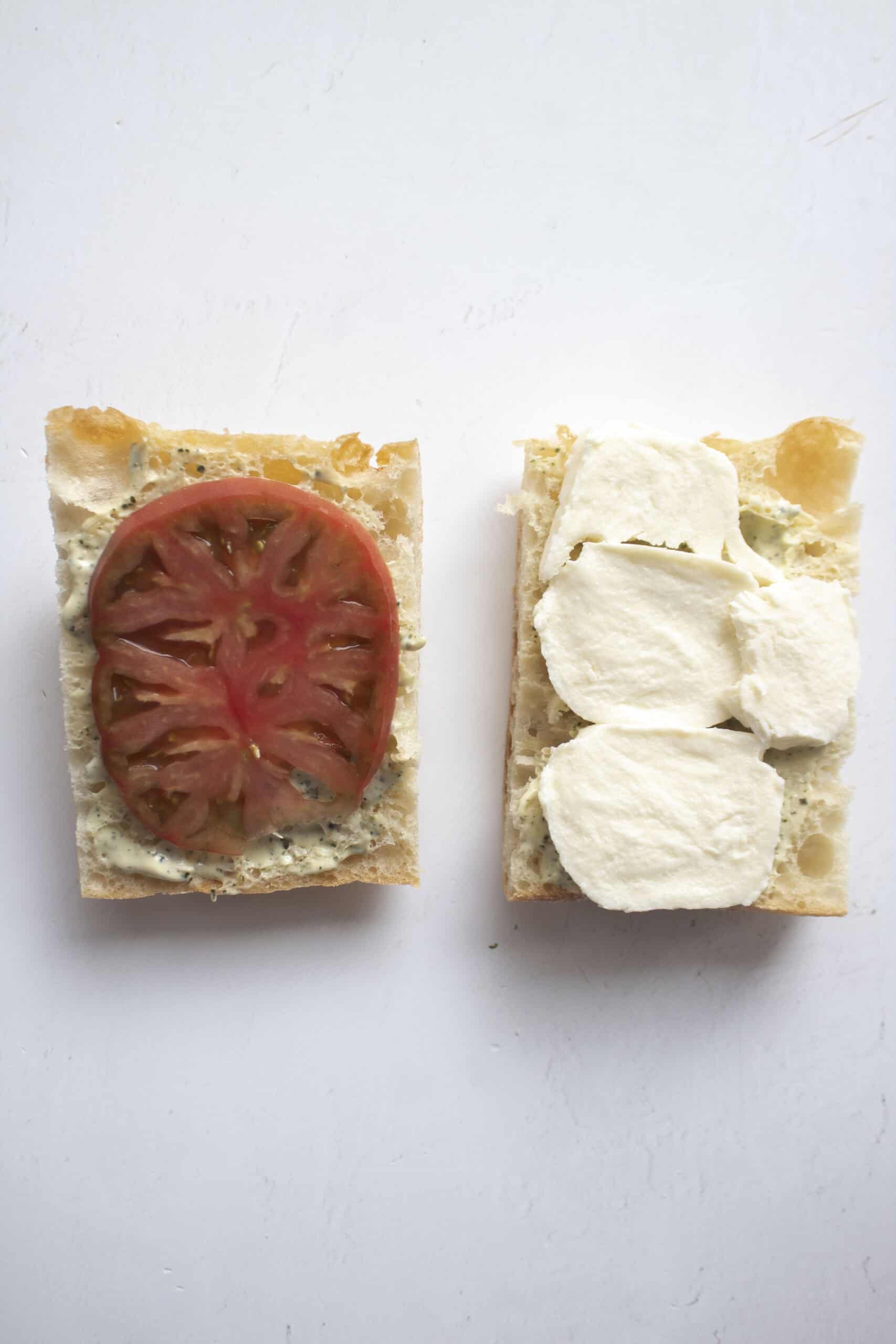 Two slices of ciabatta bread with one topped with tomato and pesto aioli, and the other with aioli and fresh mozzarella cheese.