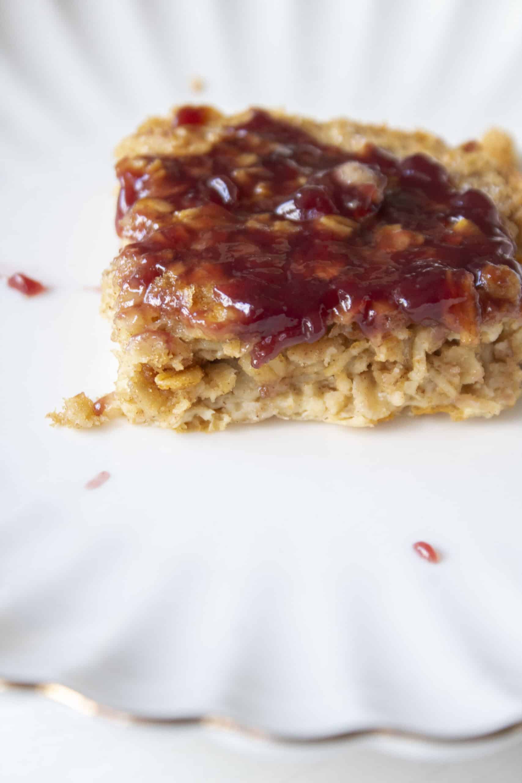 Close up of a slice of peanut butter oatmeal bake topped with grape jelly on a scalloped plate.