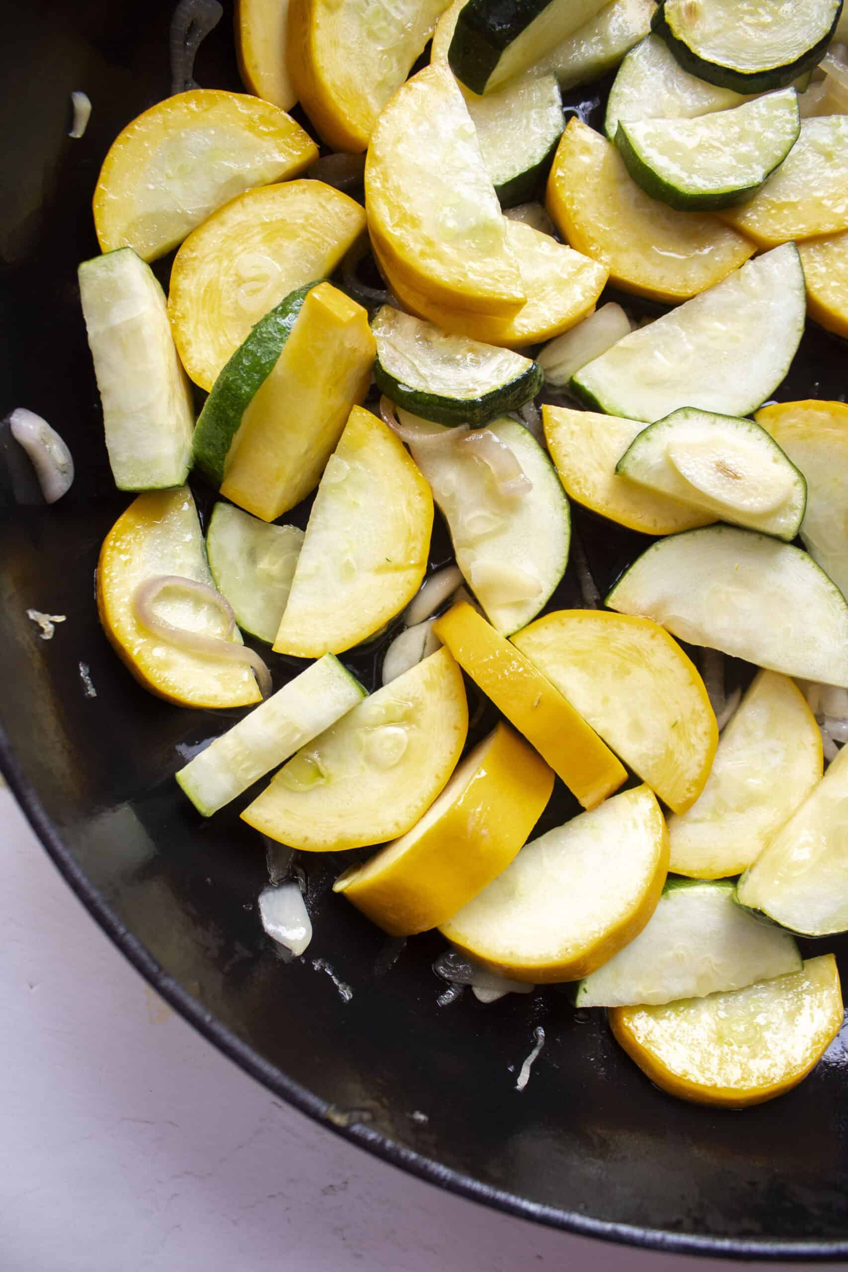 Diced and sliced zucchini and yellow squash with sauteed shallots and garlic in a large cast iron skillet.