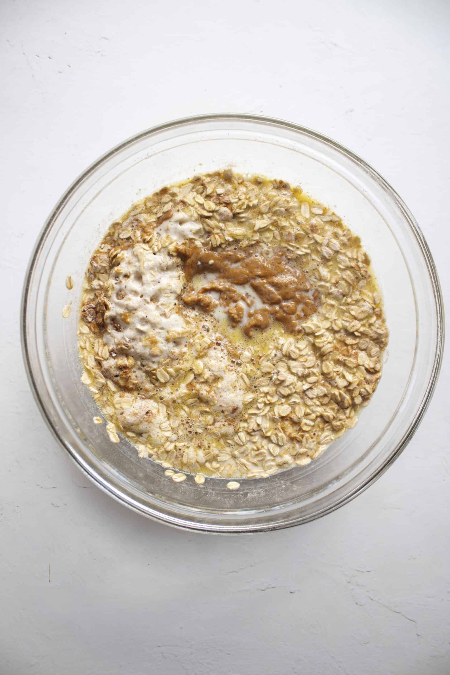 Dried rolled oats with salt, cinnamon, and baking powder combined with whisked eggs, milk, oil, and peanut butter in a mixing bowl.
