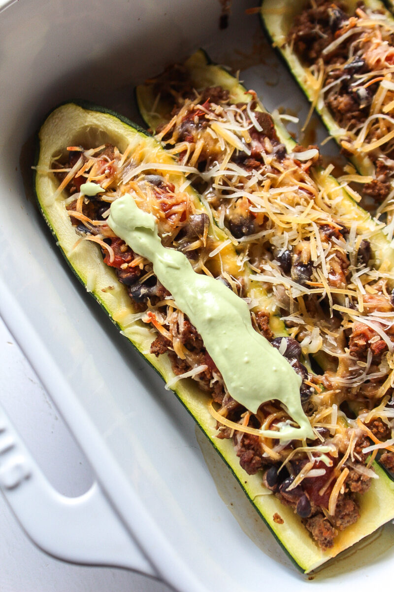Close up of a taco zucchini boat topped with avocado crema in a baking dish.