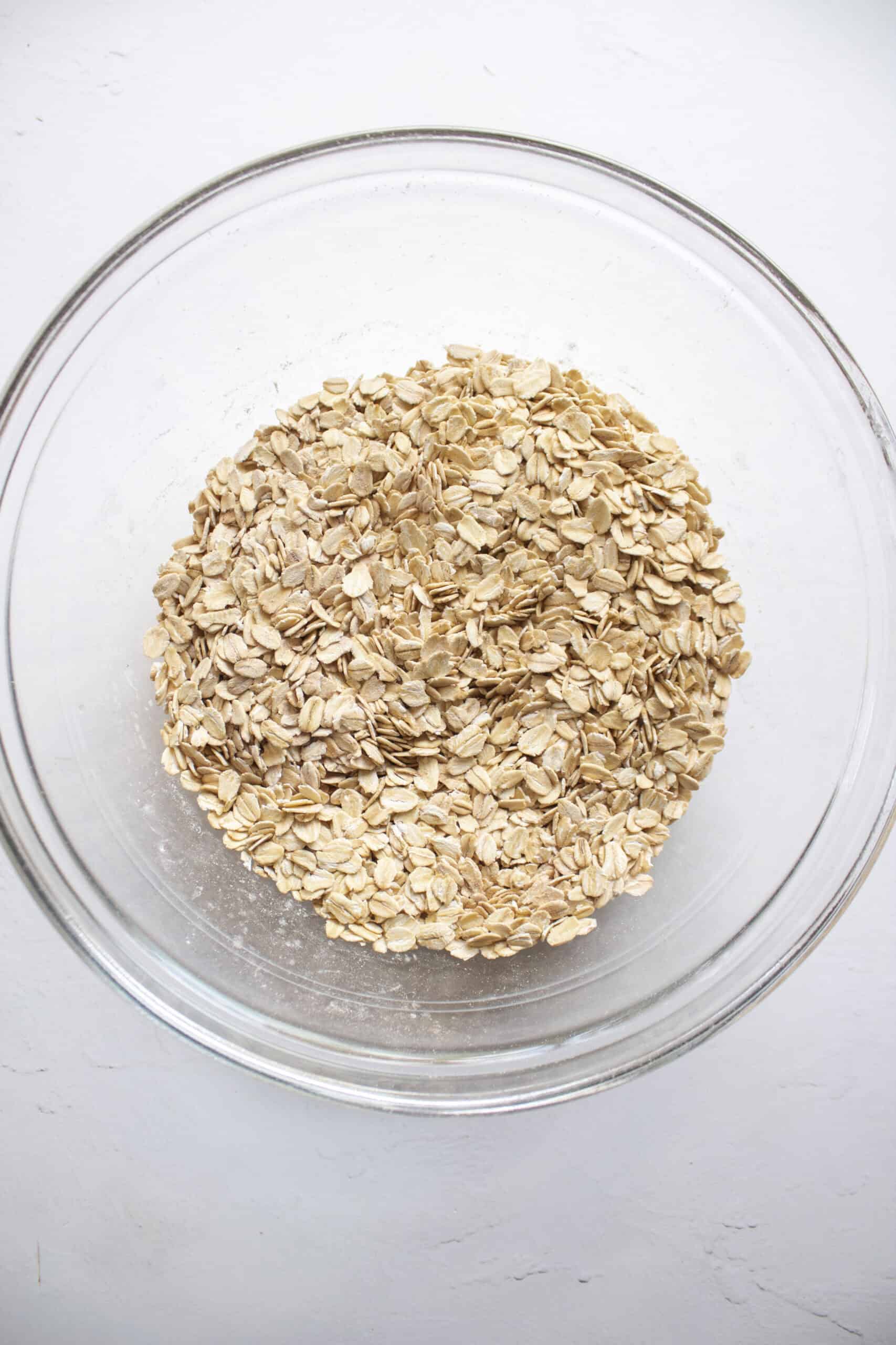 Rolled oats, baking powder, salt, and cinnamon mixed together in a glass mixing bowl.