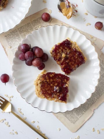 Two slices of peanut butter oatmeal bake topped with grape jelly on a scalloped plate.