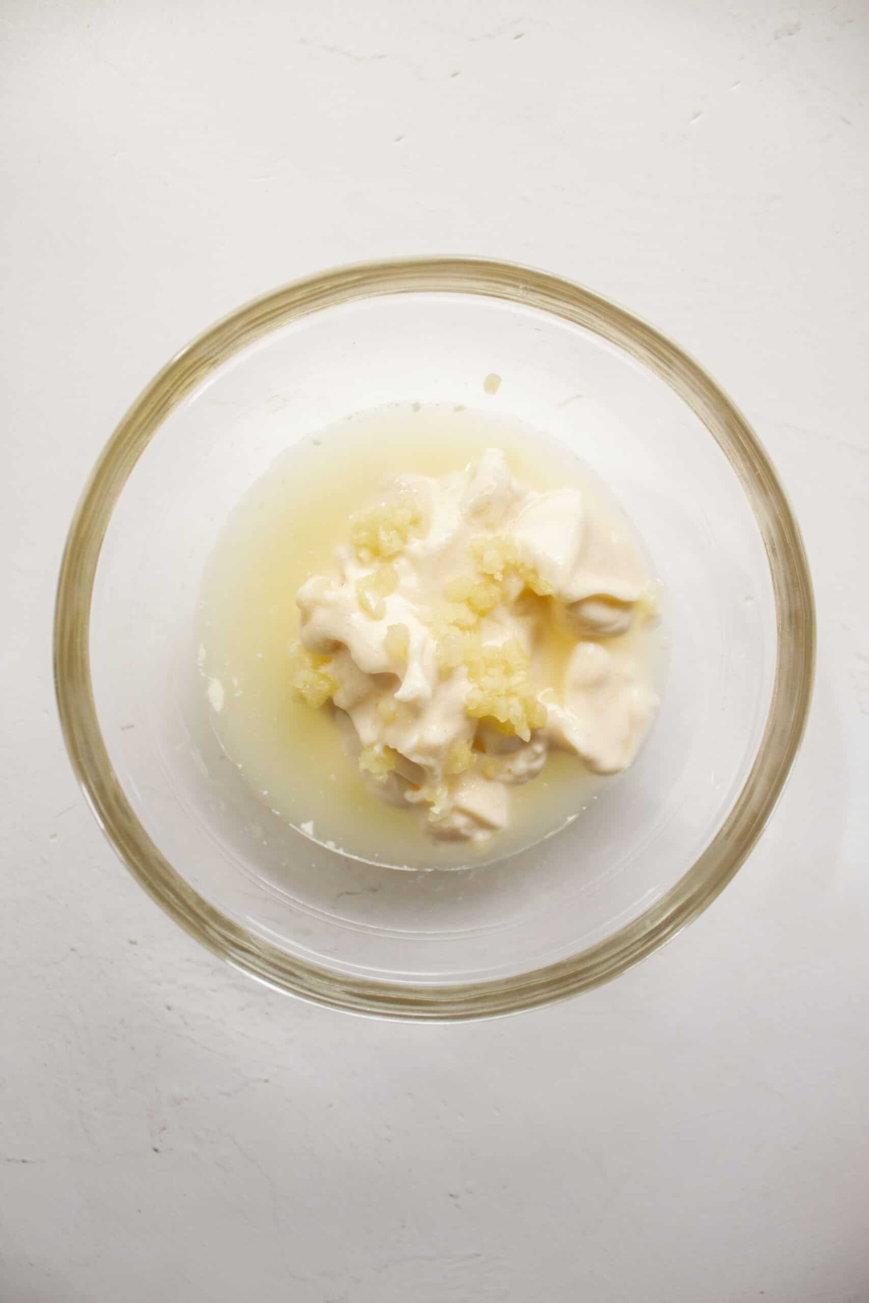 A small glass bowl with mayonnaise, garlic, garlic powder, lemon juice, and salt.