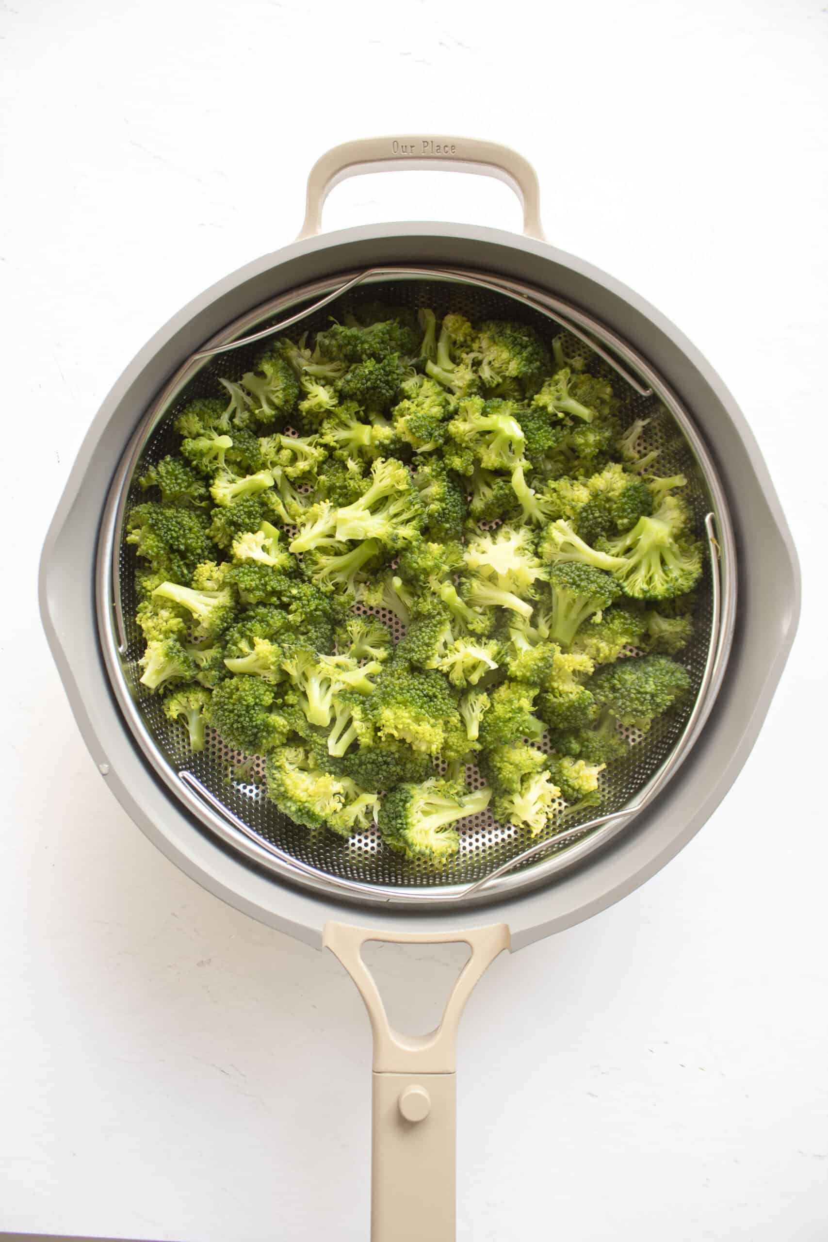 Blanched broccoli in a strainer inside a frying pan.