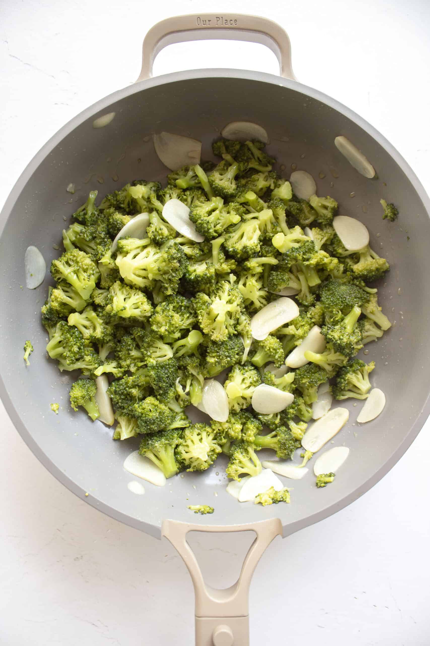Blanched broccoli tossed with garlic in a frying pan with olive oil.