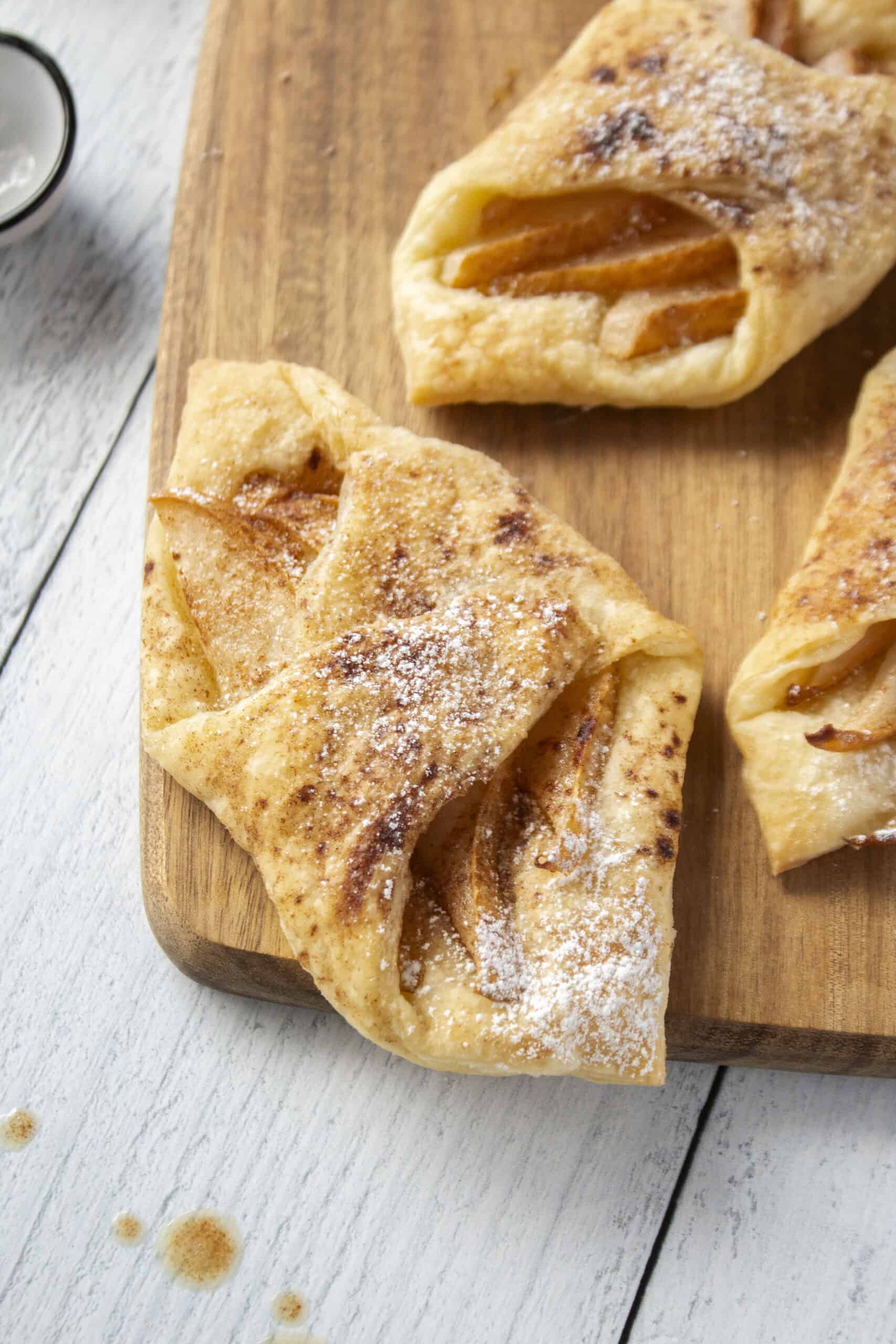 Close up of a pear and brown butter puff pastry tart on a wooden serving board.