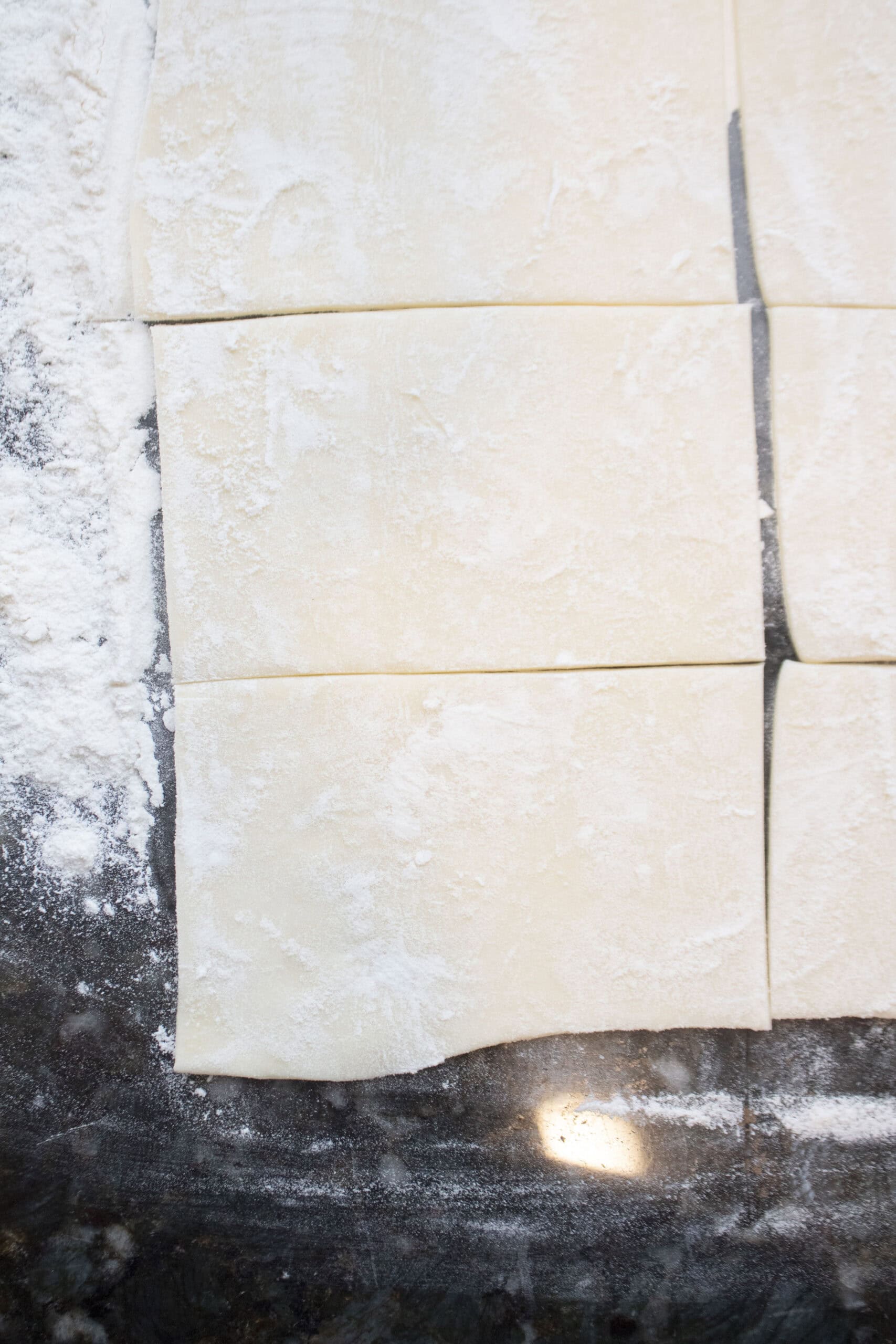 Puff pastry rolled in flour on a countertop then cut into smaller squares.