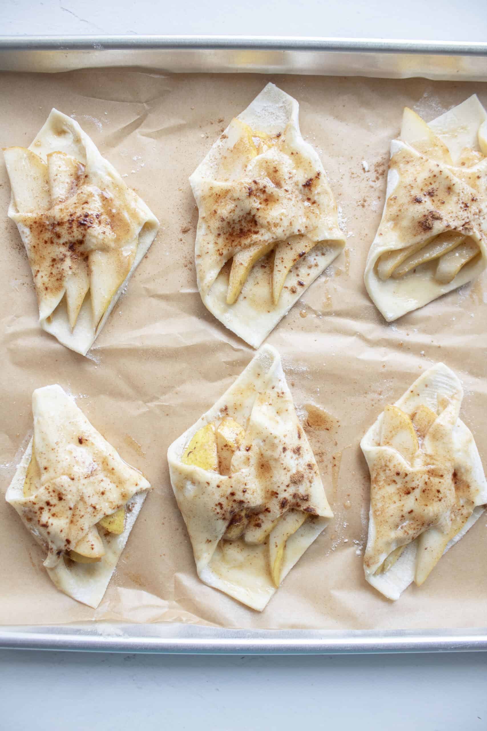 Puff pastry squares with several slices of pear on a baking sheet brushed with brown butter and cinnamon.