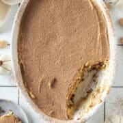 Pumpkin tiramisu with a piece of the tiramisu missing and on a plate to the side surrounded by mini white pumpkins.
