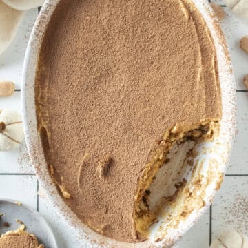 Pumpkin tiramisu with a piece of the tiramisu missing and on a plate to the side surrounded by mini white pumpkins.