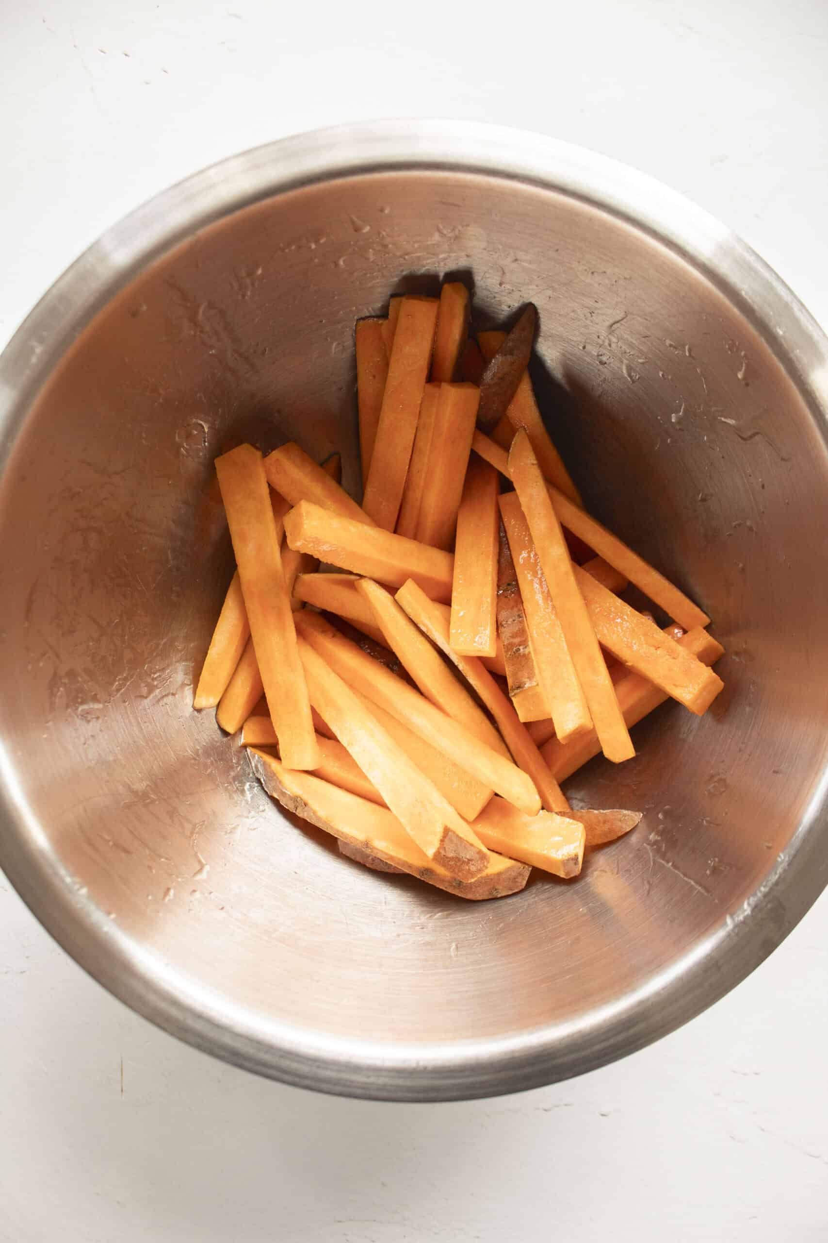 Sweet potato fries in a mixing bowl tossed with olive oil.