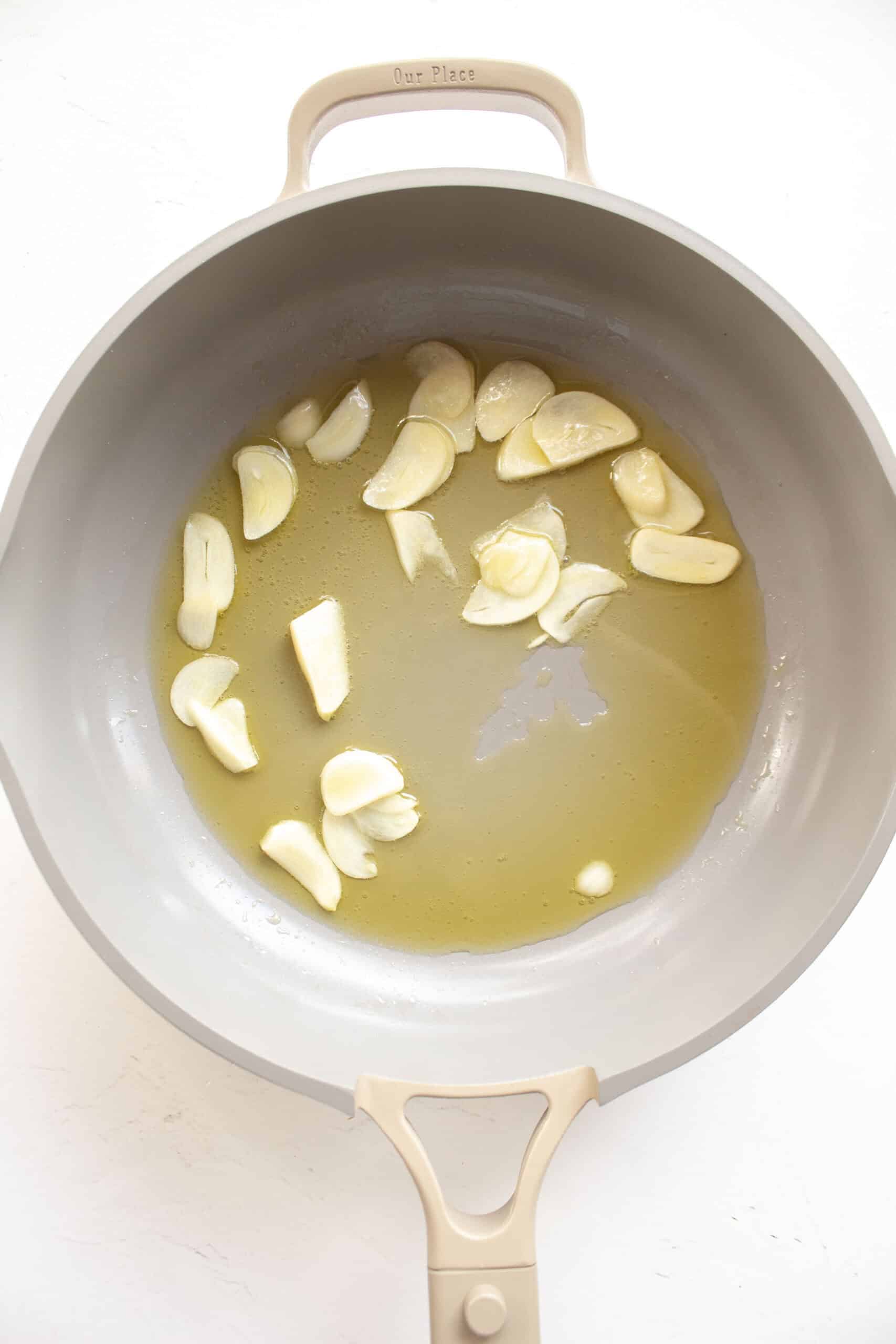 Thinly sliced garlic in a frying pan with olive oil.