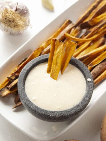 Three sweet potato fries dipped into the garlic aioli surrounded by more sweet potato fries.