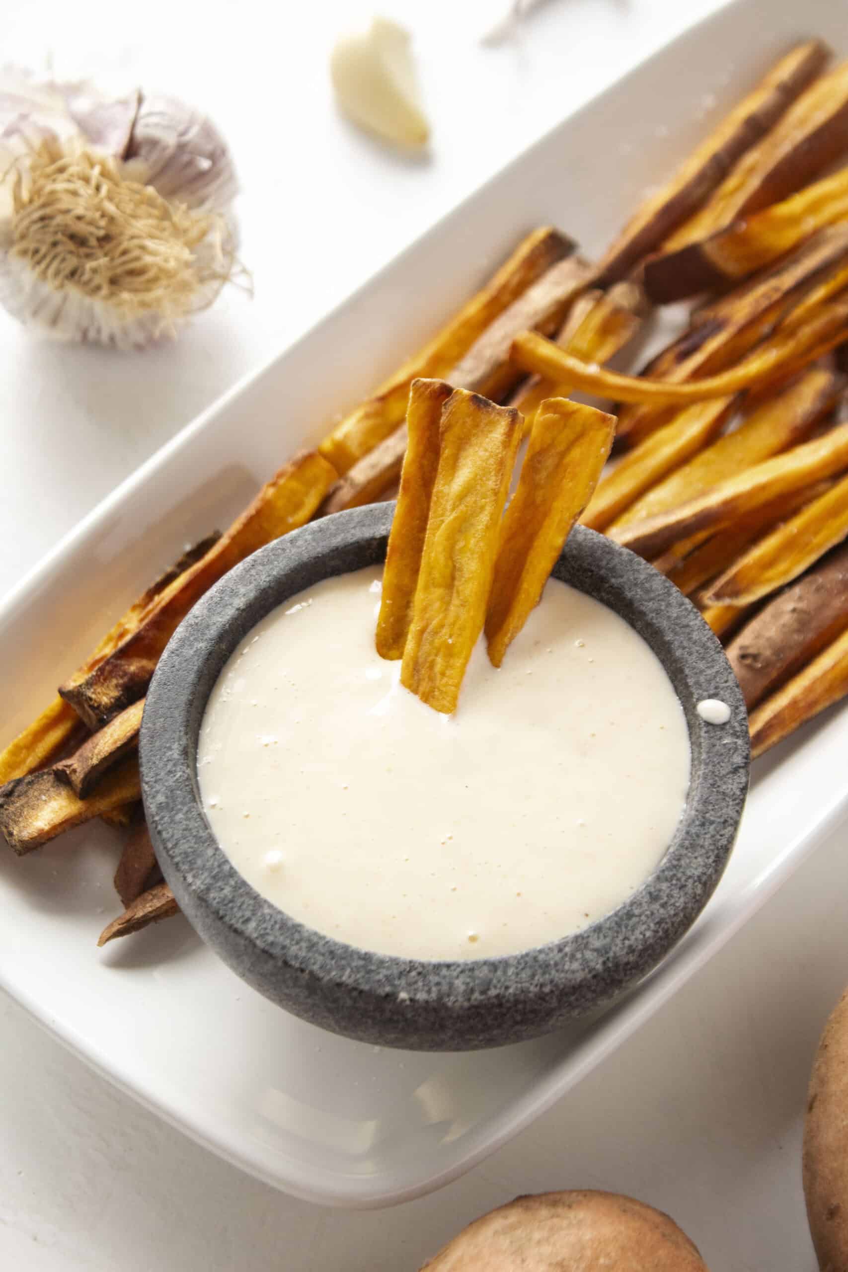 Three sweet potato fries dipped into the garlic aioli surrounded by more sweet potato fries.