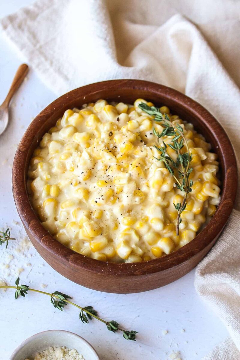 A bowl of creamed corn topped with salt and pepper and fresh thyme.