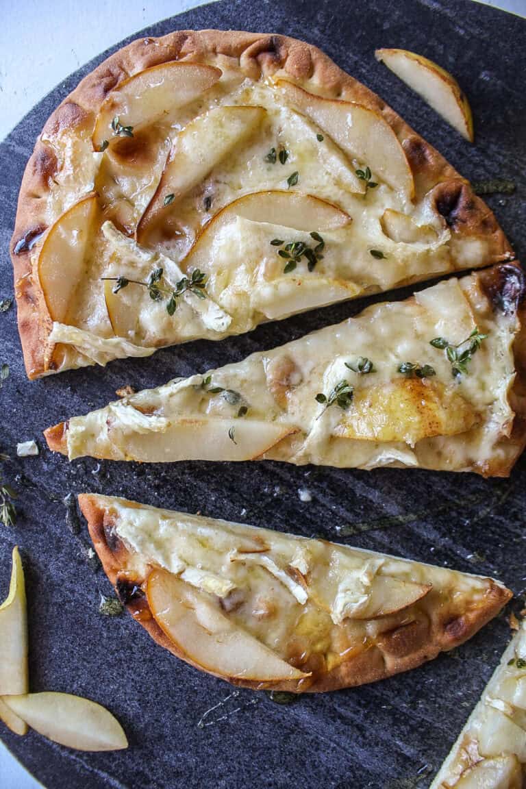 A pear and brie flatbread cut into three pieces on a marble serving board.