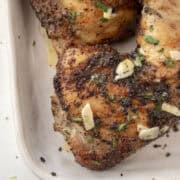 Close up baked lemon pepper chicken leg quarters topped with a melted garlic butter with parsley on a serving platter.