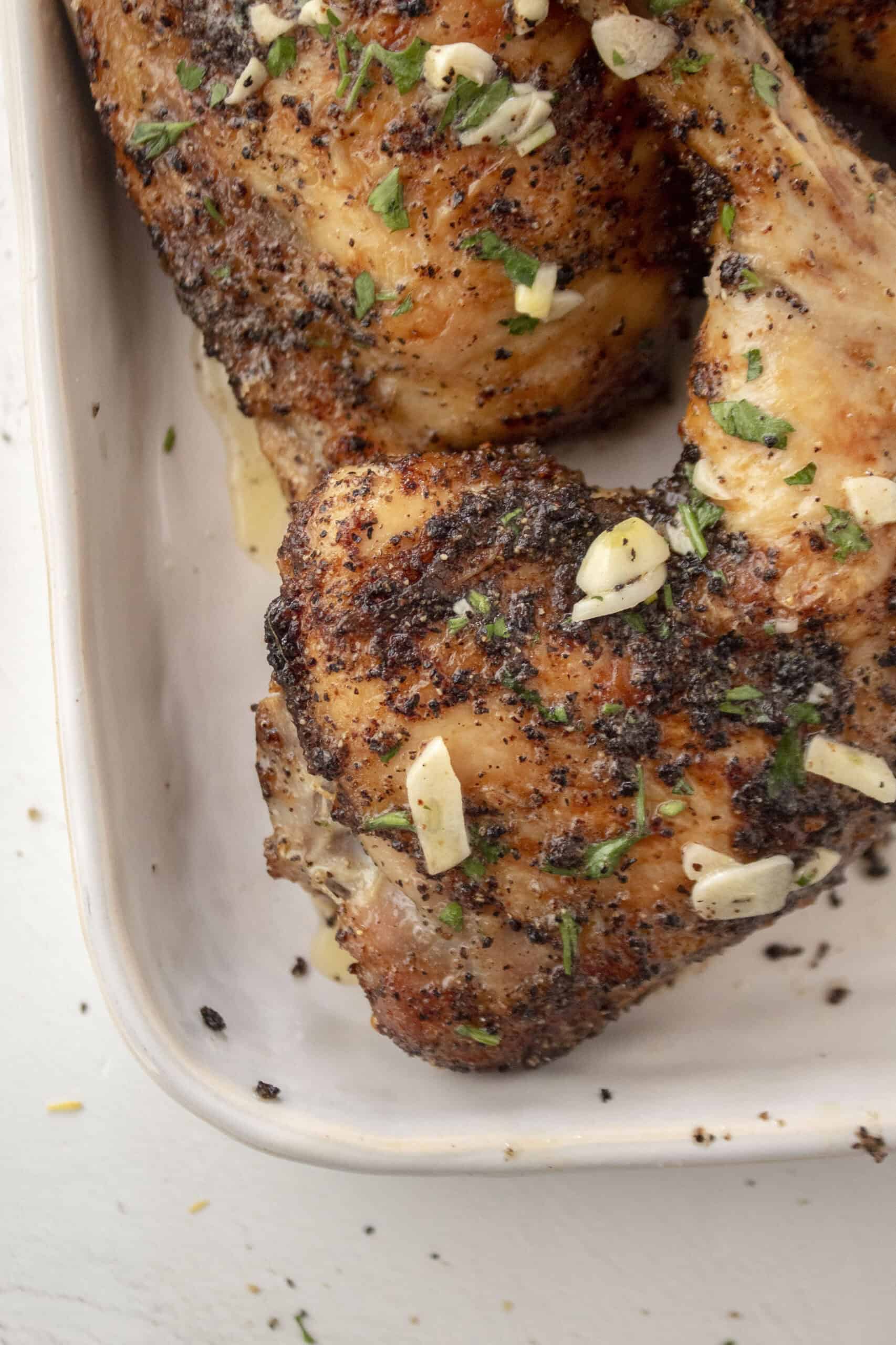 Close up baked lemon pepper chicken leg quarters topped with a melted garlic butter with parsley on a serving platter.