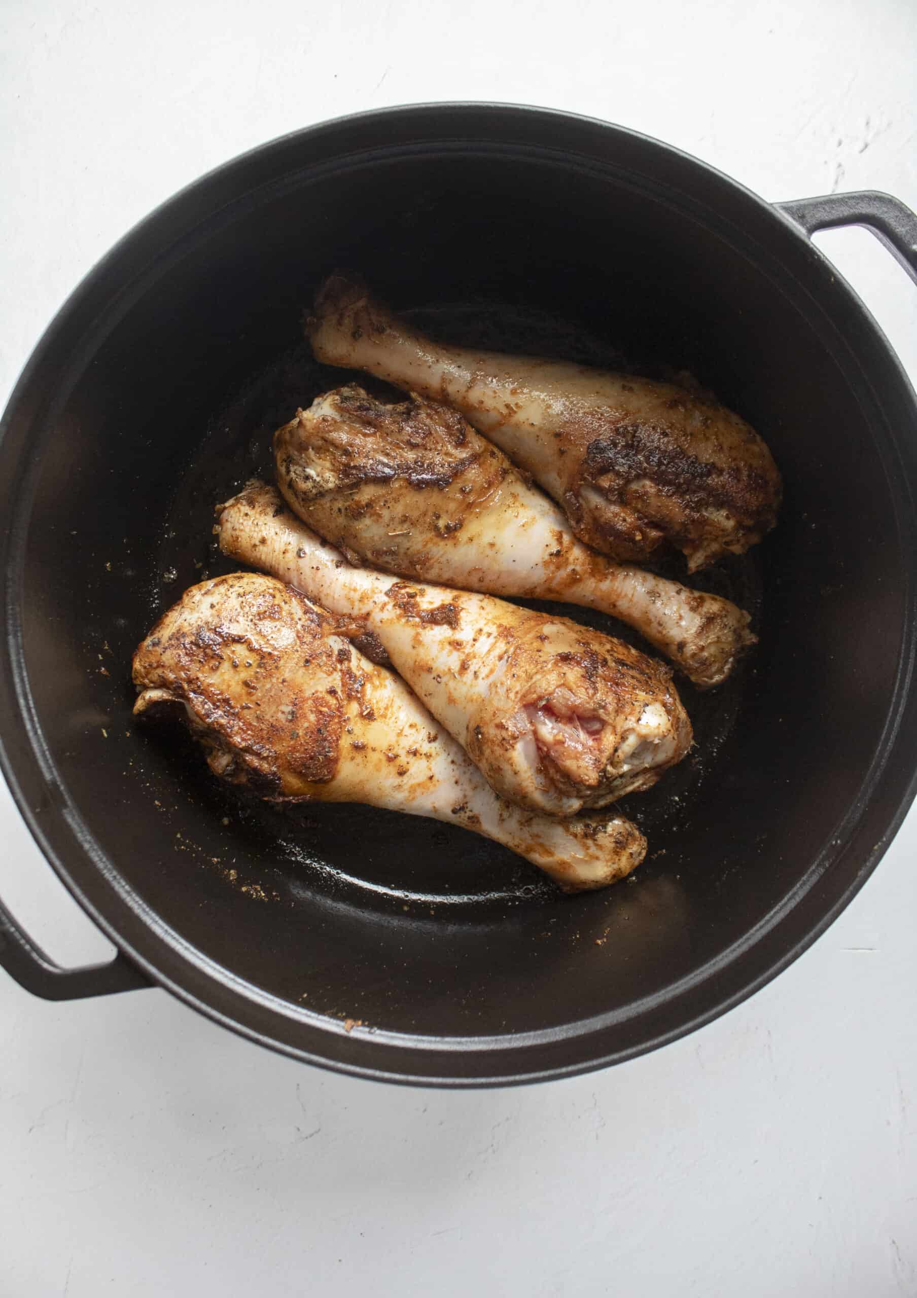 Four turkey legs seared in a large black cast iron dutch oven.