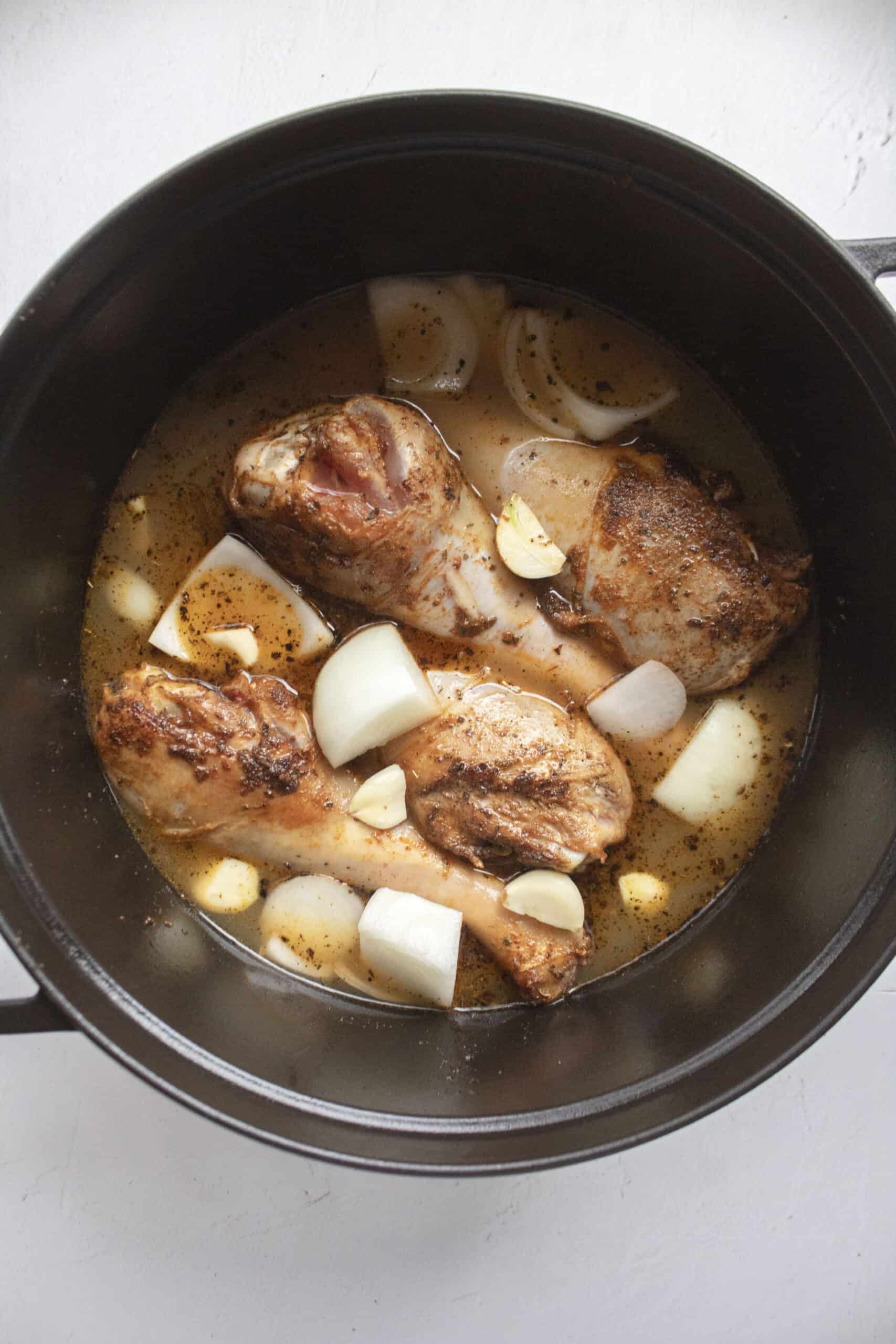 Four turkey legs seared in a large black cast iron dutch oven with apple cider, bone broth, chopped onions, and garlic.