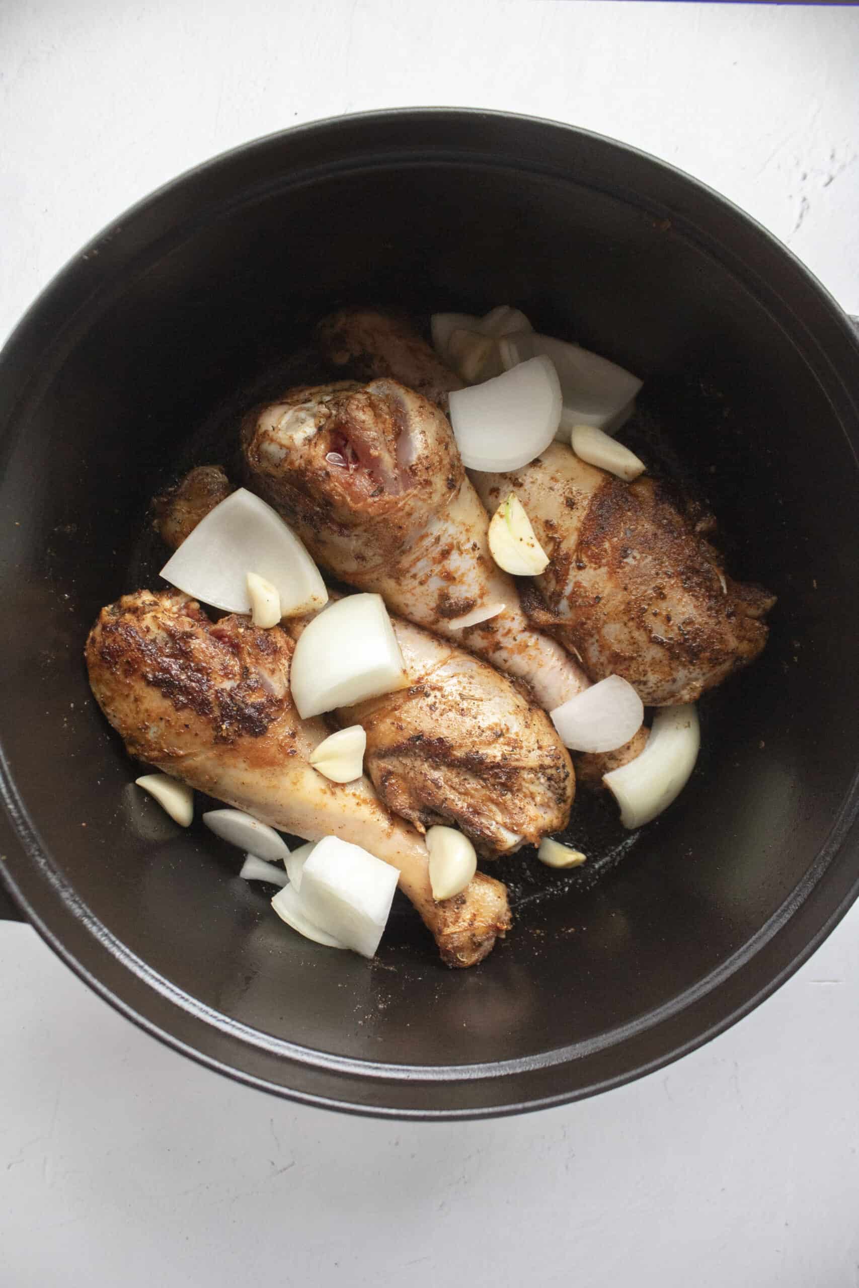 Four turkey legs seared in a large black dutch oven with chopped onions and garlic.